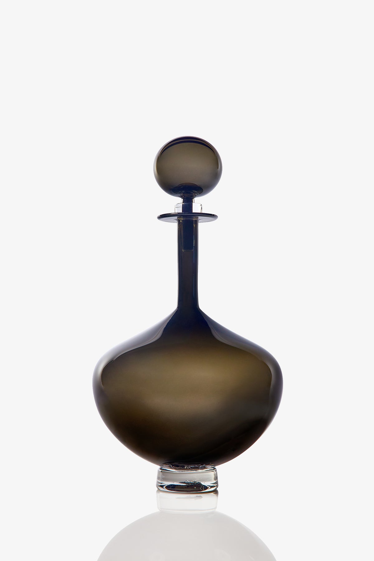 The Petite Genie Bottle Decanter features dark, smoky glass with a wide rounded base, a long narrow neck, and a spherical stopper, displayed against a white background.