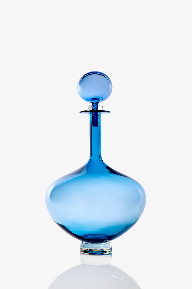 The Petite Genie Bottle Decanter features blue glass with a wide, rounded base, narrow neck, and matching round stopper, displayed against a plain white background.