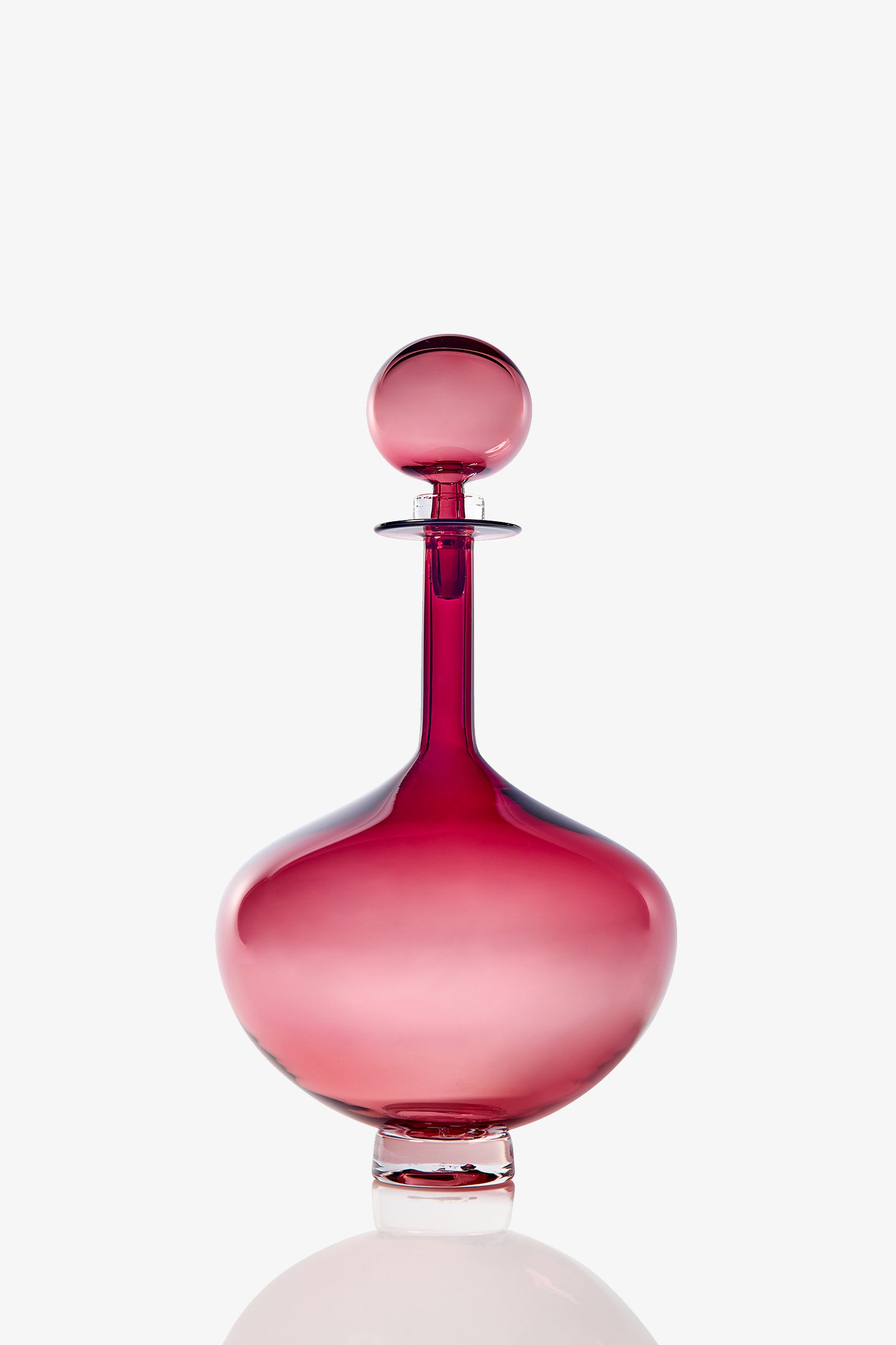 The Petite Genie Bottle Decanter features a sleek, round glass design in a deep pink hue with a matching spherical stopper, showcased against a plain white background.