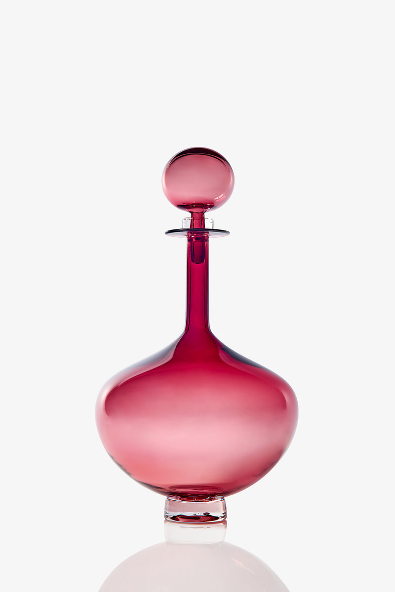 The Petite Genie Bottle Decanter features a sleek, round glass design in a deep pink hue with a matching spherical stopper, showcased against a plain white background.