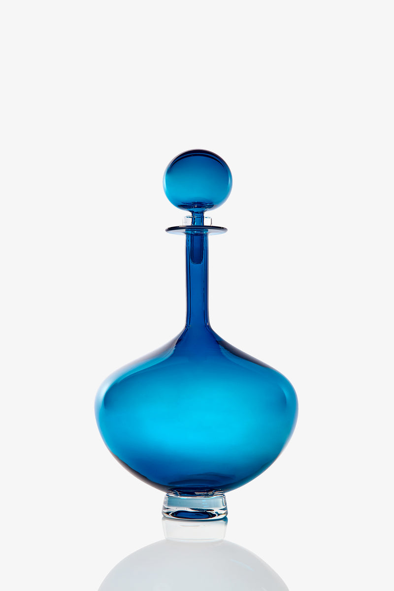 The Petite Genie Bottle Decanter features blue glass with a round stopper, wide base, and narrow neck, displayed on a white background.