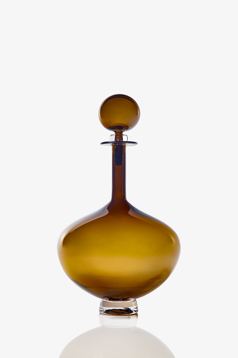 The Petite Genie Bottle Decanter is a round, amber glass decanter with a wide base, slender neck, and matching spherical stopper, shown against a plain white background.