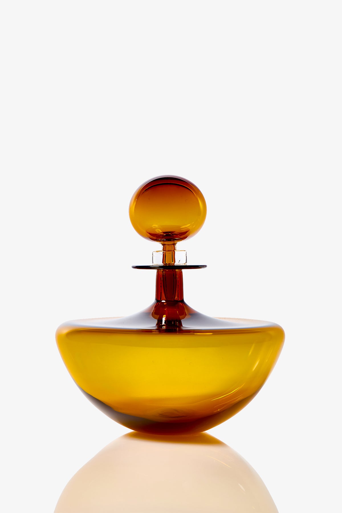 A glossy, amber Small Angelic Bottle with a round stopper sits on a plain white background. The glass bottle has a wide, rounded base and a narrow neck.