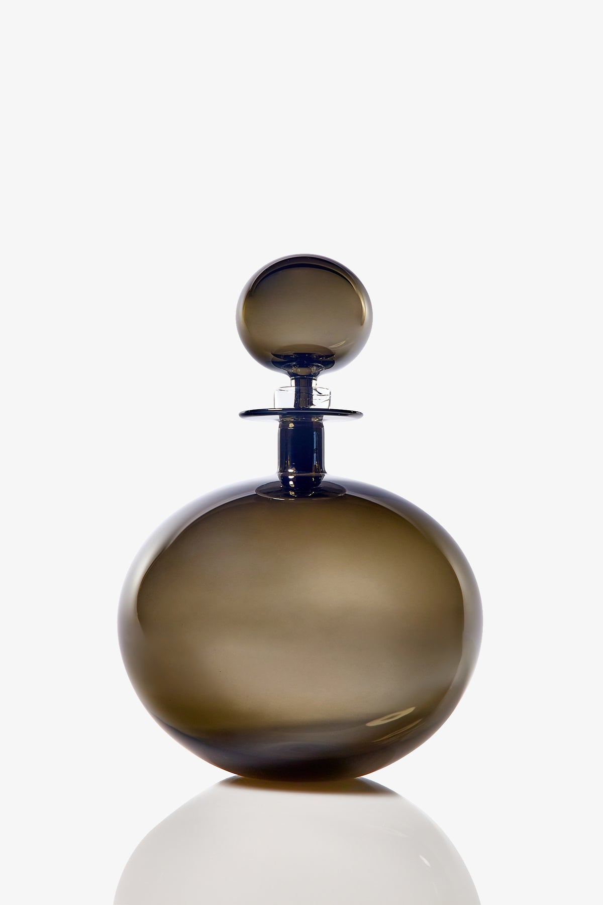 The Small Angelic Bottle is a round, smoky glass perfume bottle with a matching stopper. Set against a white background, its smooth, glossy surface casts a faint reflection below.