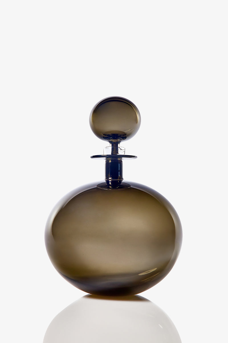 The Small Angelic Bottle is a round, smoky glass perfume bottle with a matching stopper. Set against a white background, its smooth, glossy surface casts a faint reflection below.