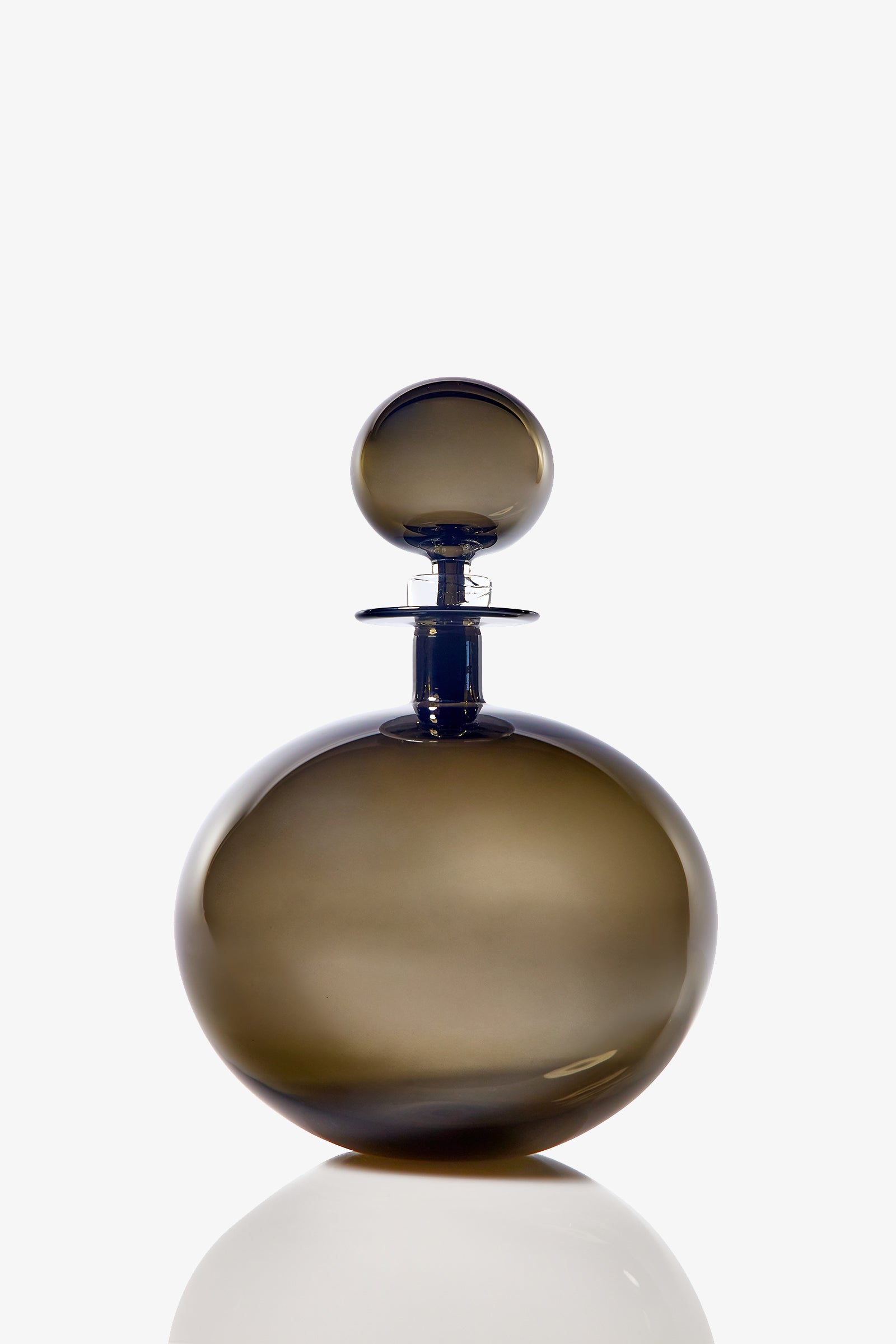 The Small Angelic Bottle is a round, smoky glass perfume bottle with a matching stopper. Set against a white background, its smooth, glossy surface casts a faint reflection below.