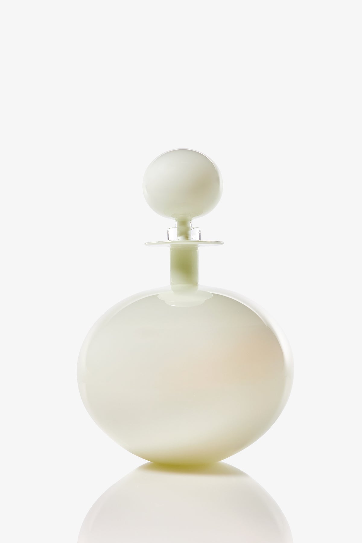 A Petite Low Round Decanter, featuring a round white bottle with a matching spherical cap, sits on a plain white background with a subtle reflection at its base.