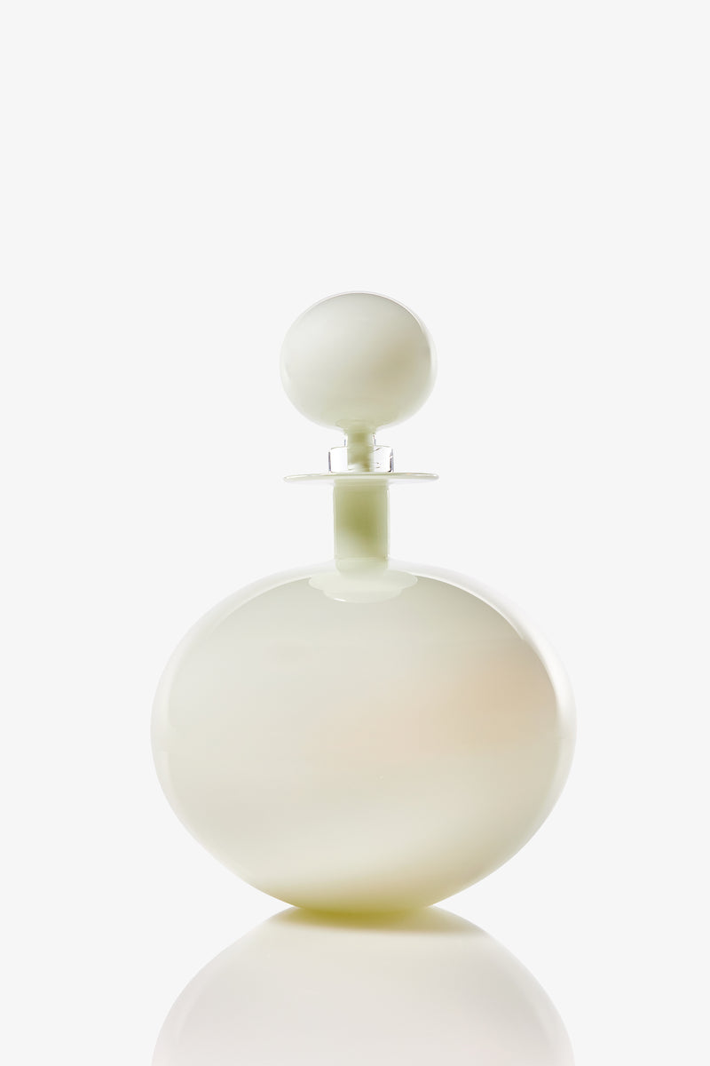 A Petite Low Round Decanter, featuring a round white bottle with a matching spherical cap, sits on a plain white background with a subtle reflection at its base.