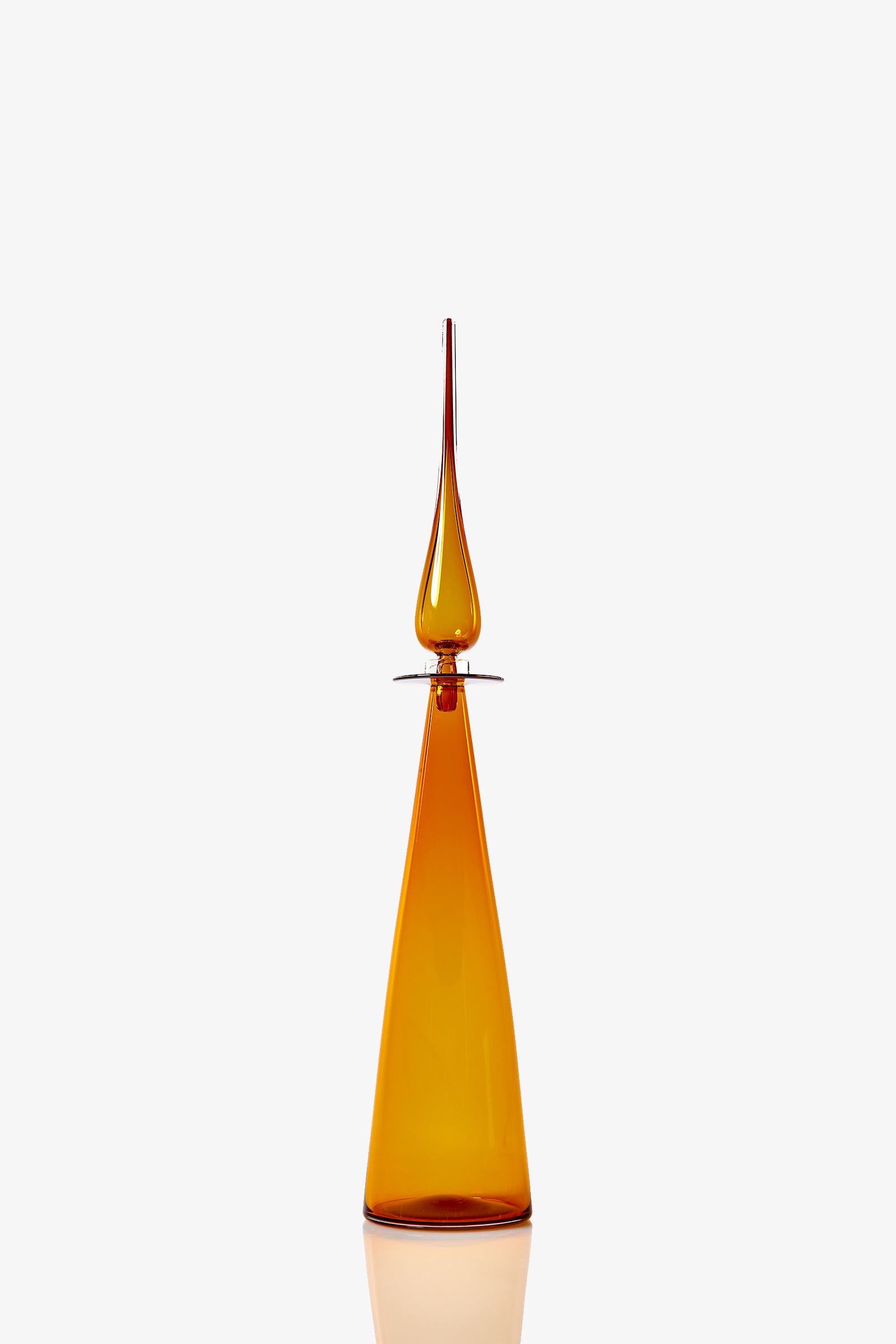 The Petite Straight Cone Decanter is a tall amber glass bottle with a geometric triangular base and slender pointed stopper, shown against a plain white background.
