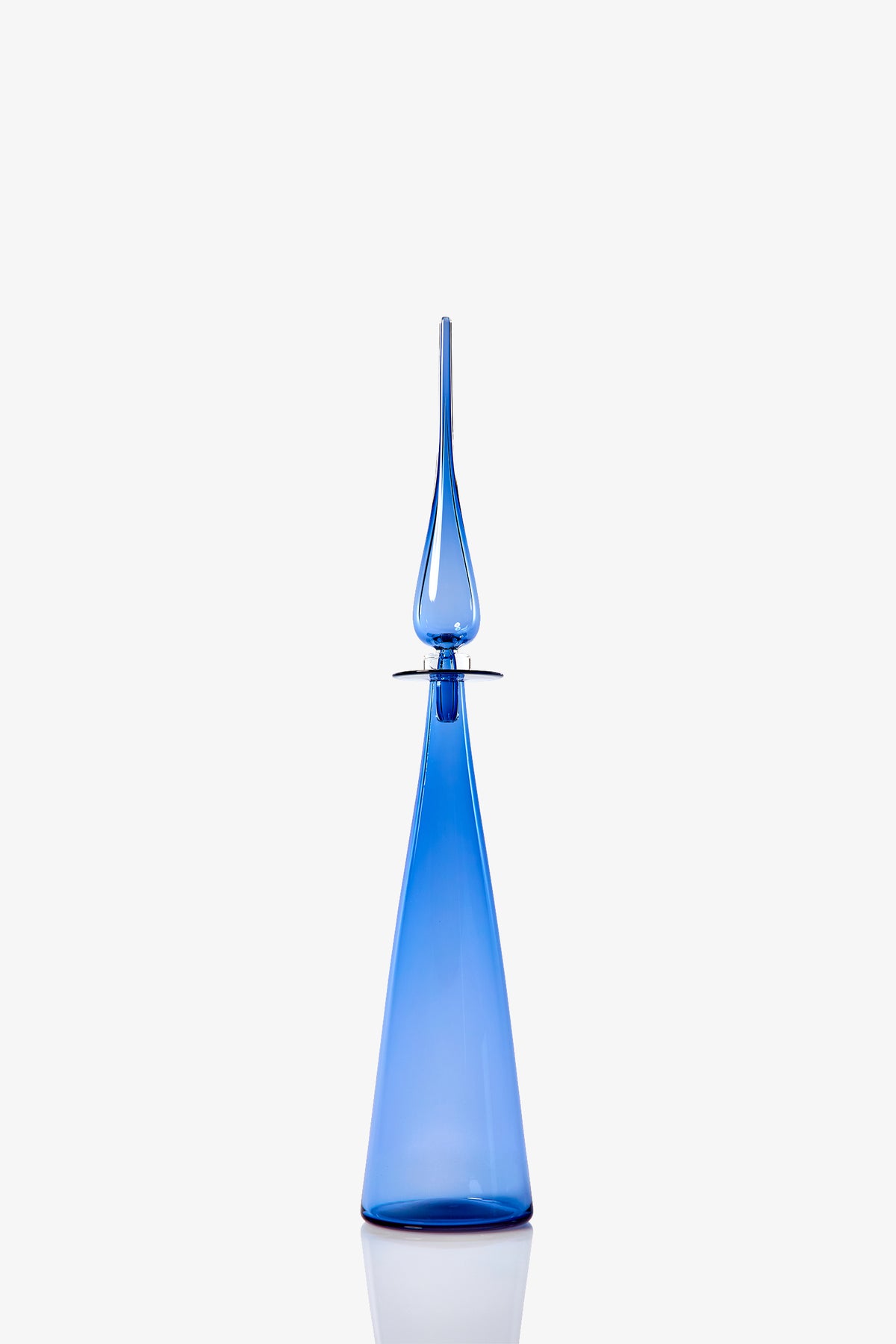 The Petite Straight Cone Decanter, a tall and elegant blue glass bottle with a pointed stopper, features a sleek modern design, smooth curves, and a glossy finish. It is displayed against a plain white background.