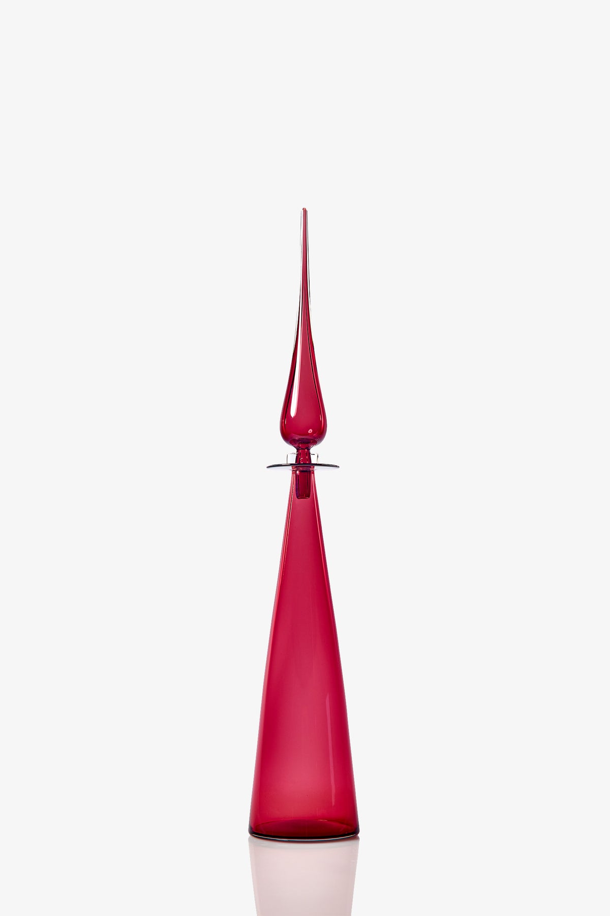The Petite Straight Cone Decanter is a tall, elegant deep red glass bottle featuring a narrow base, pointed stopper, and reflective surface, showcased against a plain white background.