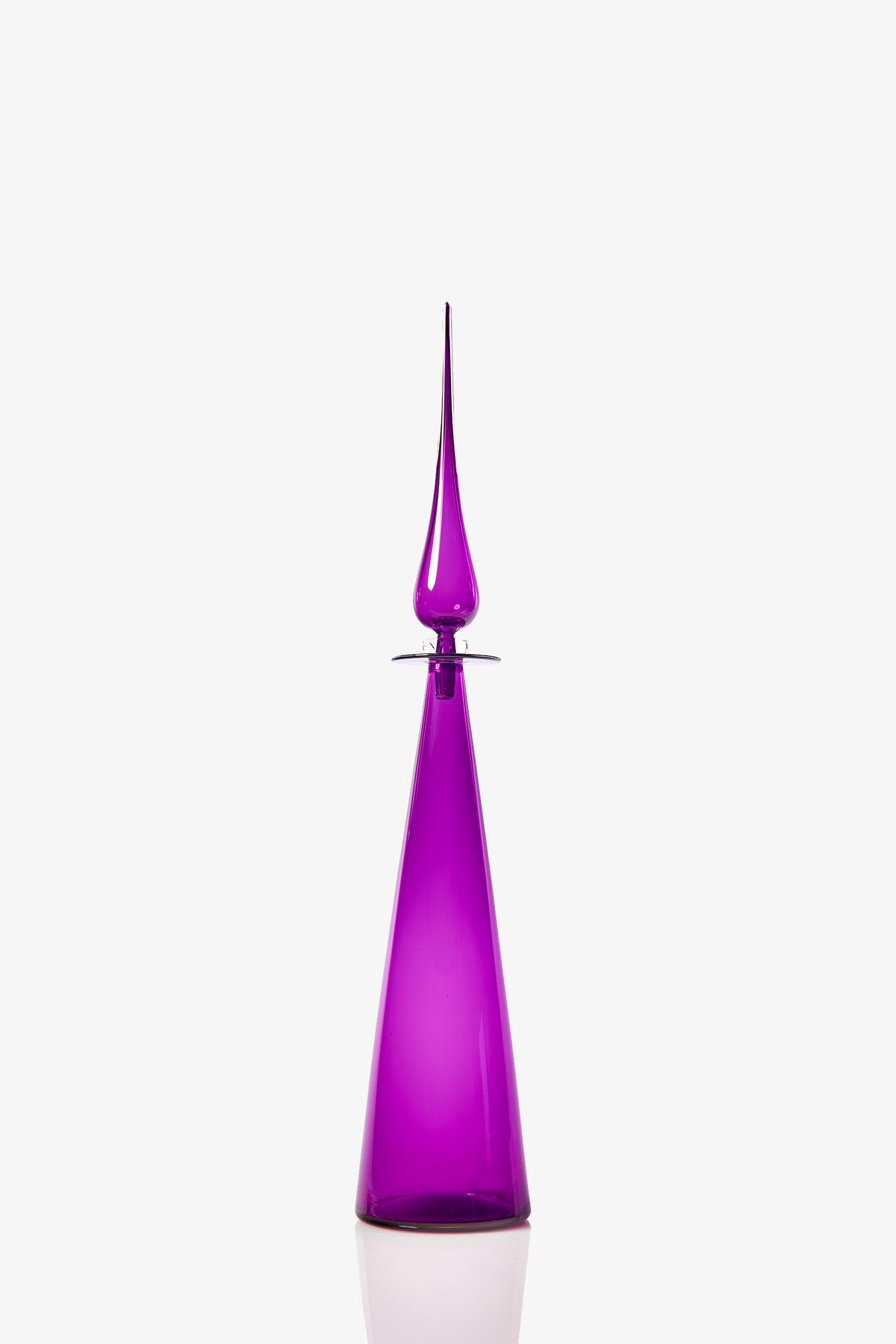The Petite Straight Cone Decanter is a tall, sleek, purple glass bottle with a pointed, sculpted stopper, shown against a plain white background.