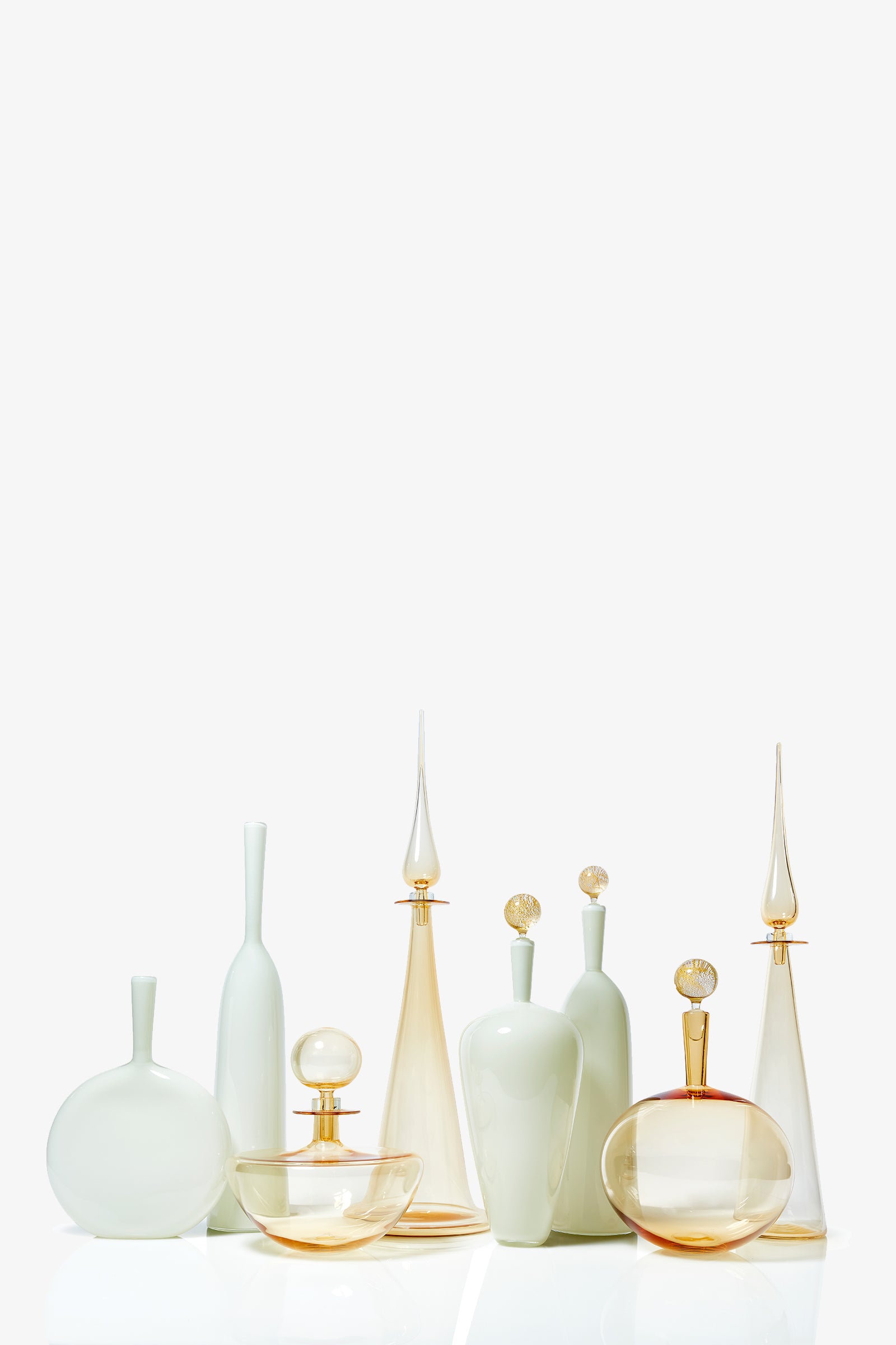 The Petite Straight Cone Decanter is an elegant glass bottle in soft white, cream, and amber tones, featuring a tall, slender stopper. Its refined shape stands out when arranged on a white surface against a plain background.