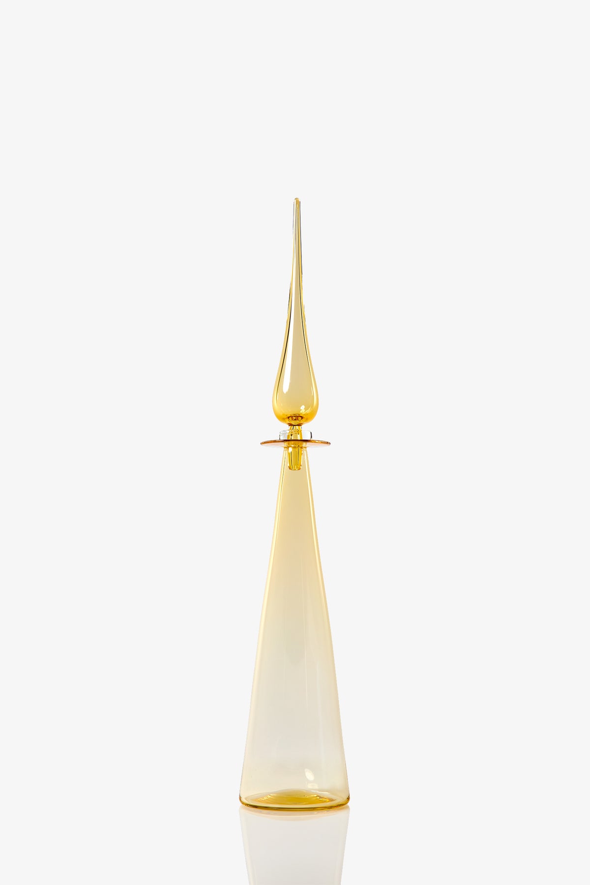 The Petite Straight Cone Decanter is a tall, elegant glass bottle with a pointed stopper in translucent amber-yellow, set against a plain white background.