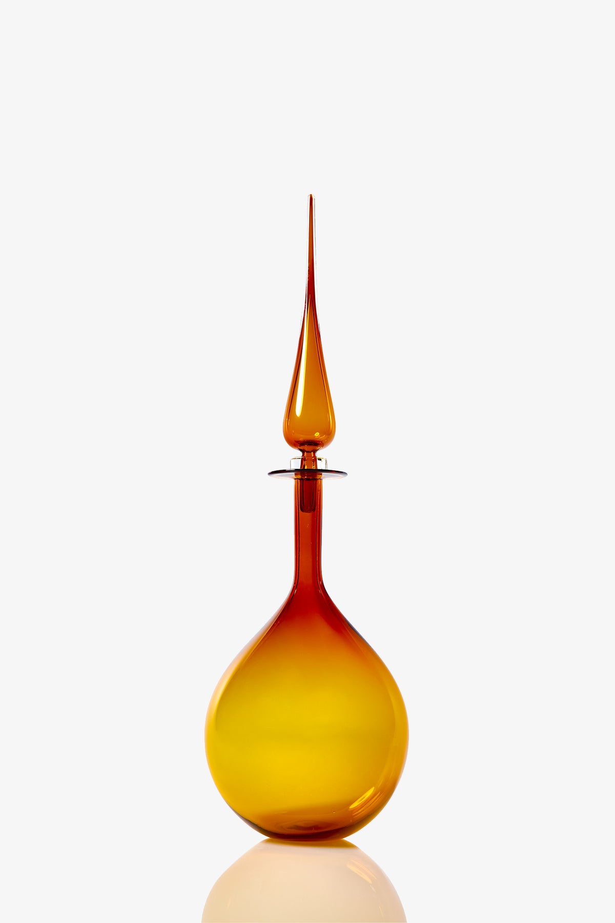 The Petite Tear Drop Decanter features a tall, amber glass body with a round base and a long, pointed stopper, showcased against a white background.