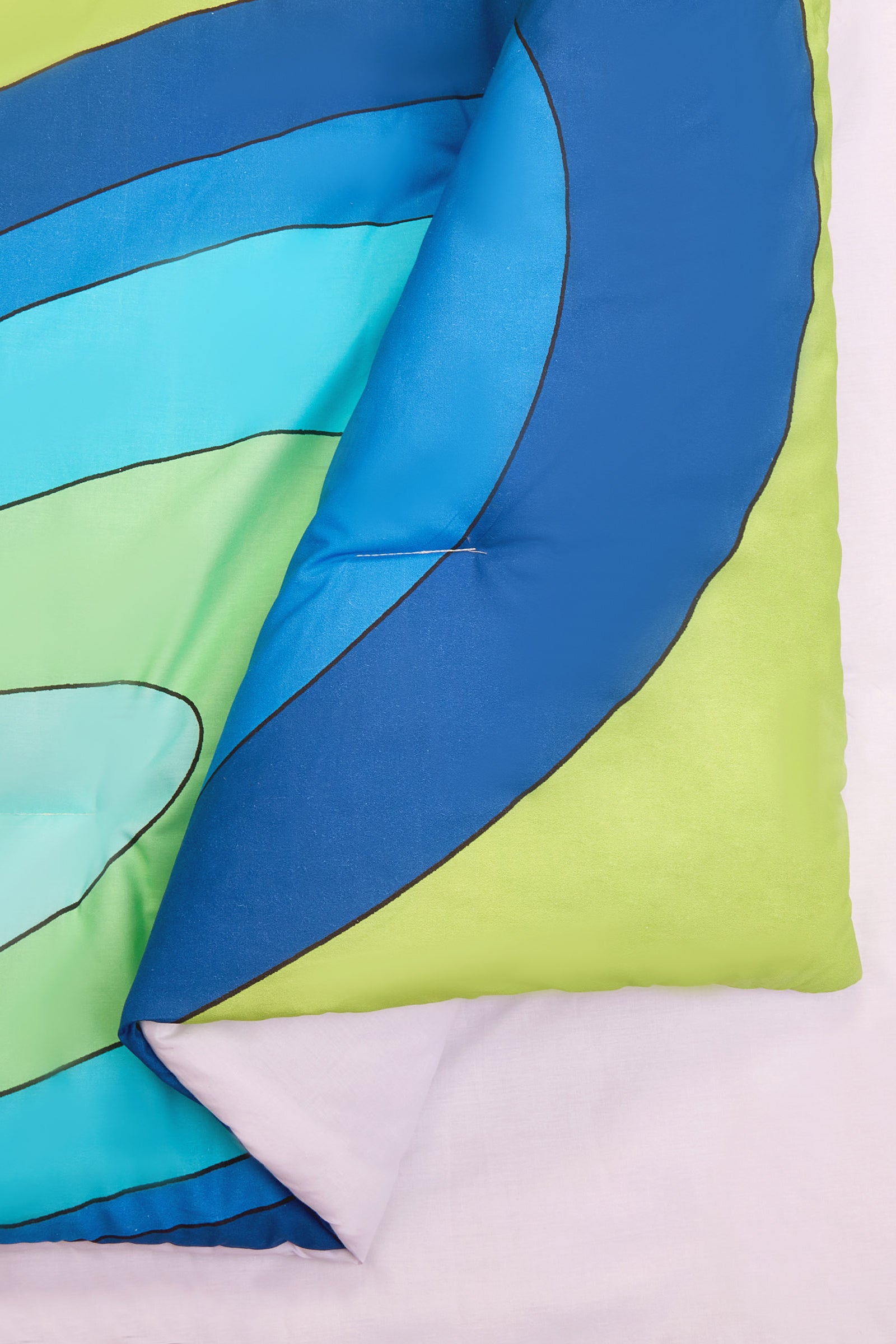 A close-up of the Wynwood Waves Full/Queen 3-Piece Comforter Set shows its wavy blue, green, and aqua patterns, partially folded over on a light pink surface.