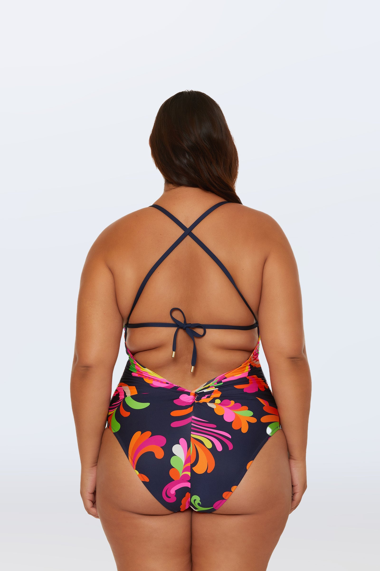 A woman wearing the Twist Back One-Piece Swimsuit in Palms Paradise, featuring a vibrant palm print and crisscross back straps, is shown from behind against a plain white background.