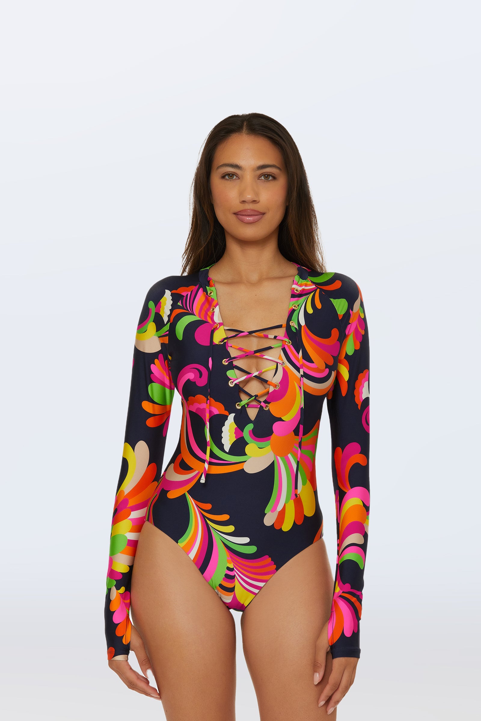 A woman models the Long-Sleeve Paddle Suit – Palms Paradise in a multi-color abstract pattern, featuring a lace-up front, against a light background.