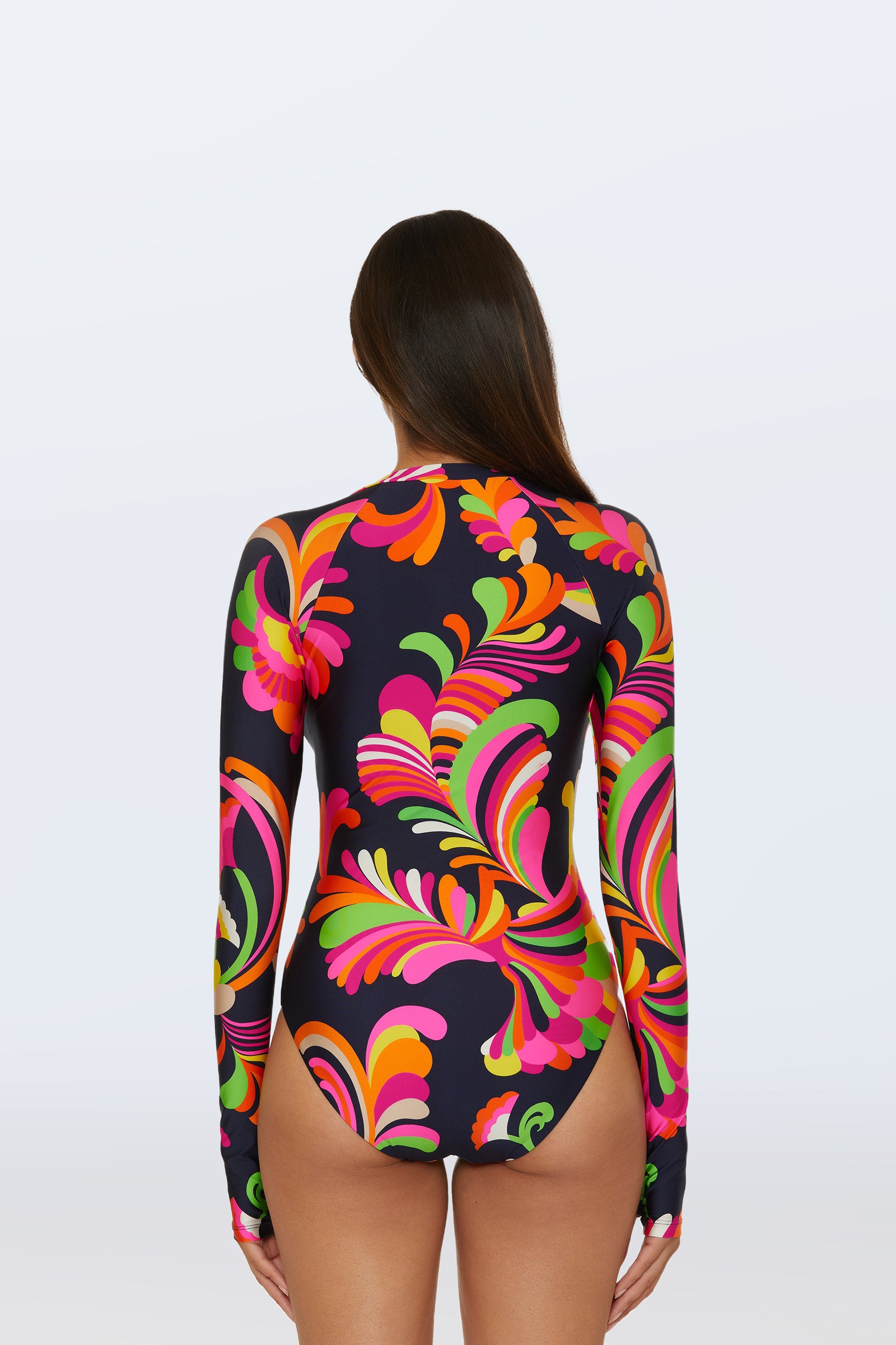 A woman with long brown hair, seen from behind, models the Long-Sleeve Paddle Suit - Palms Paradise, featuring a high neck and a vibrant pink, orange, green, and yellow swirling floral pattern on a dark background.