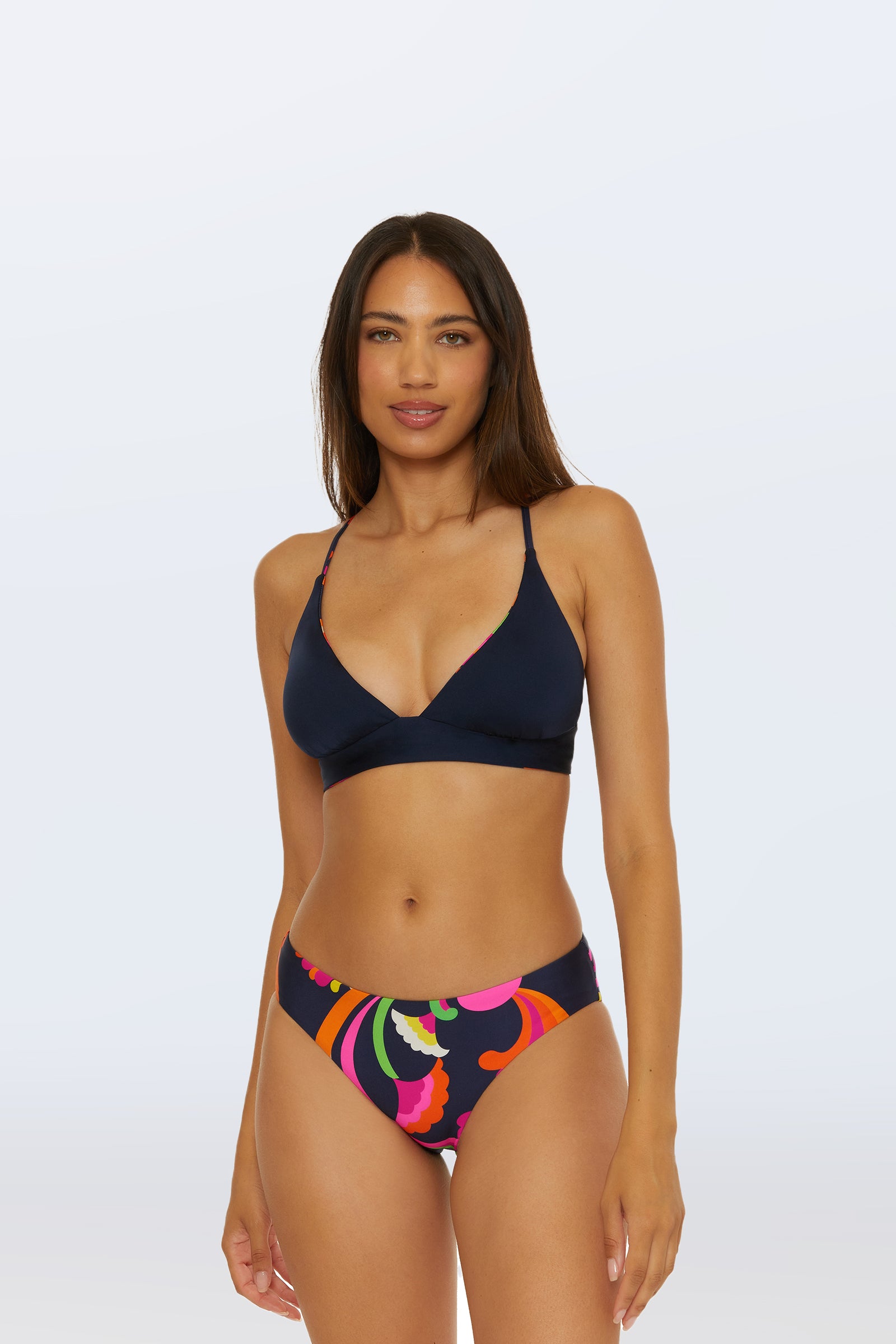 A woman faces forward wearing the Reversible Halter Bra Swim Top - Palms Paradise in navy blue, paired with colorful, swirl-patterned bikini bottoms against a plain light background.