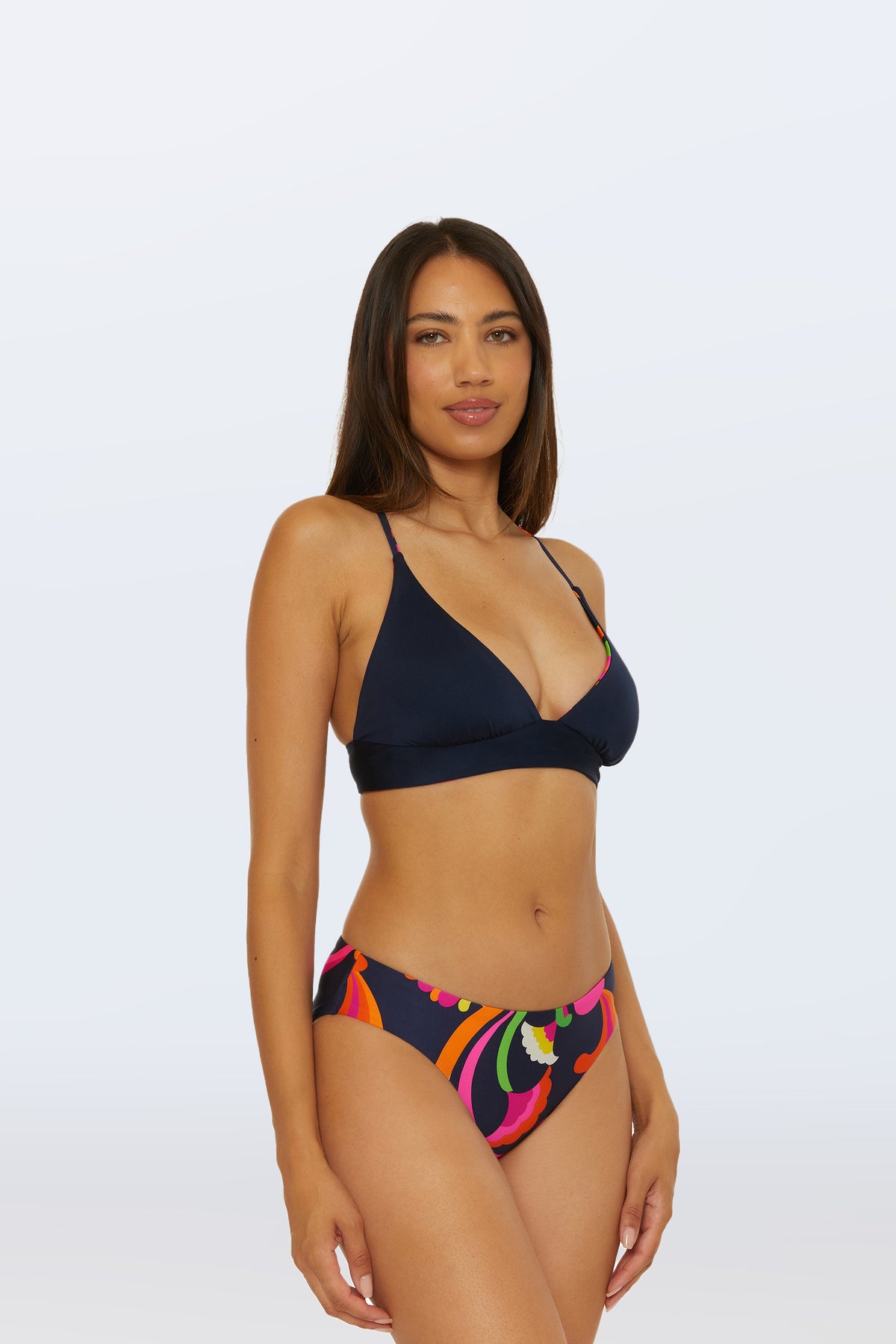 A woman with long, straight brown hair wears the Reversible Halter Bra Swim Top - Palms Paradise. She stands against a plain, light background, facing slightly to the side and looking at the camera.