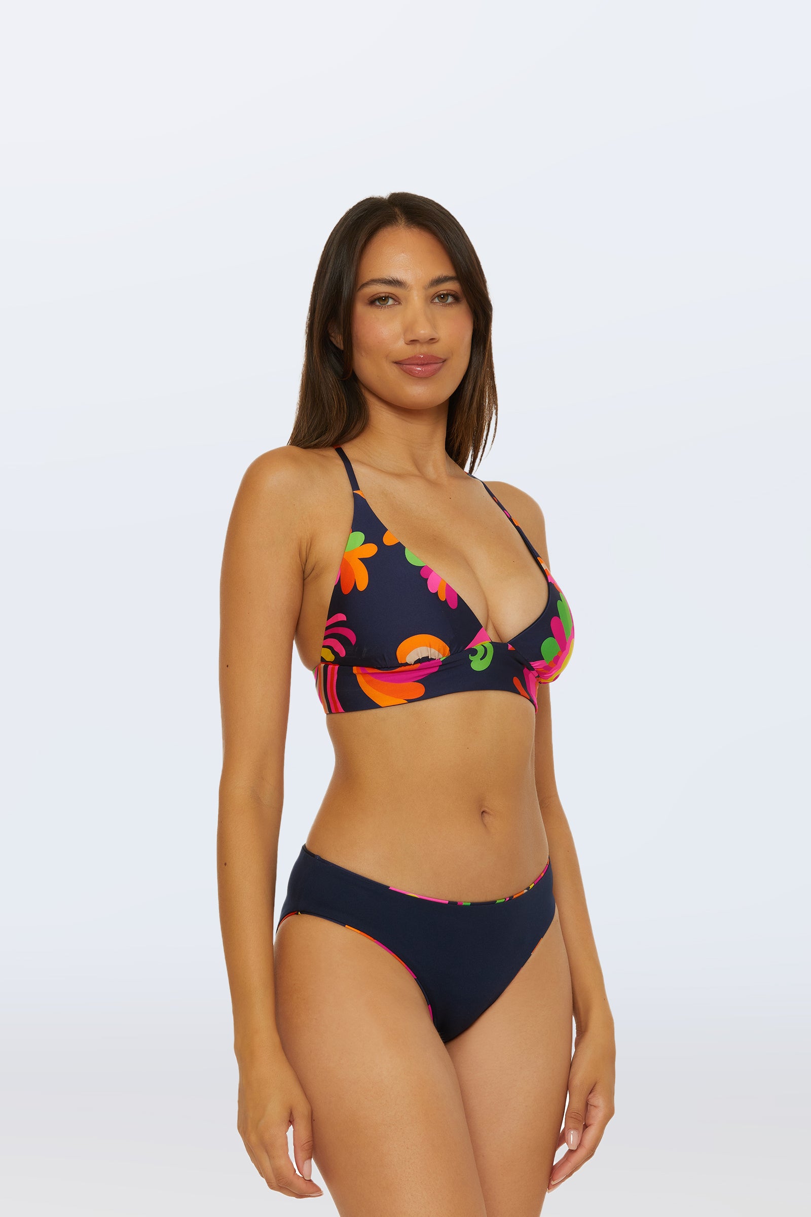 A woman stands against a plain light background, smiling softly and facing slightly to the side, wearing the Reversible Hipster Bottom - Palms Paradise in a navy blue floral pattern.