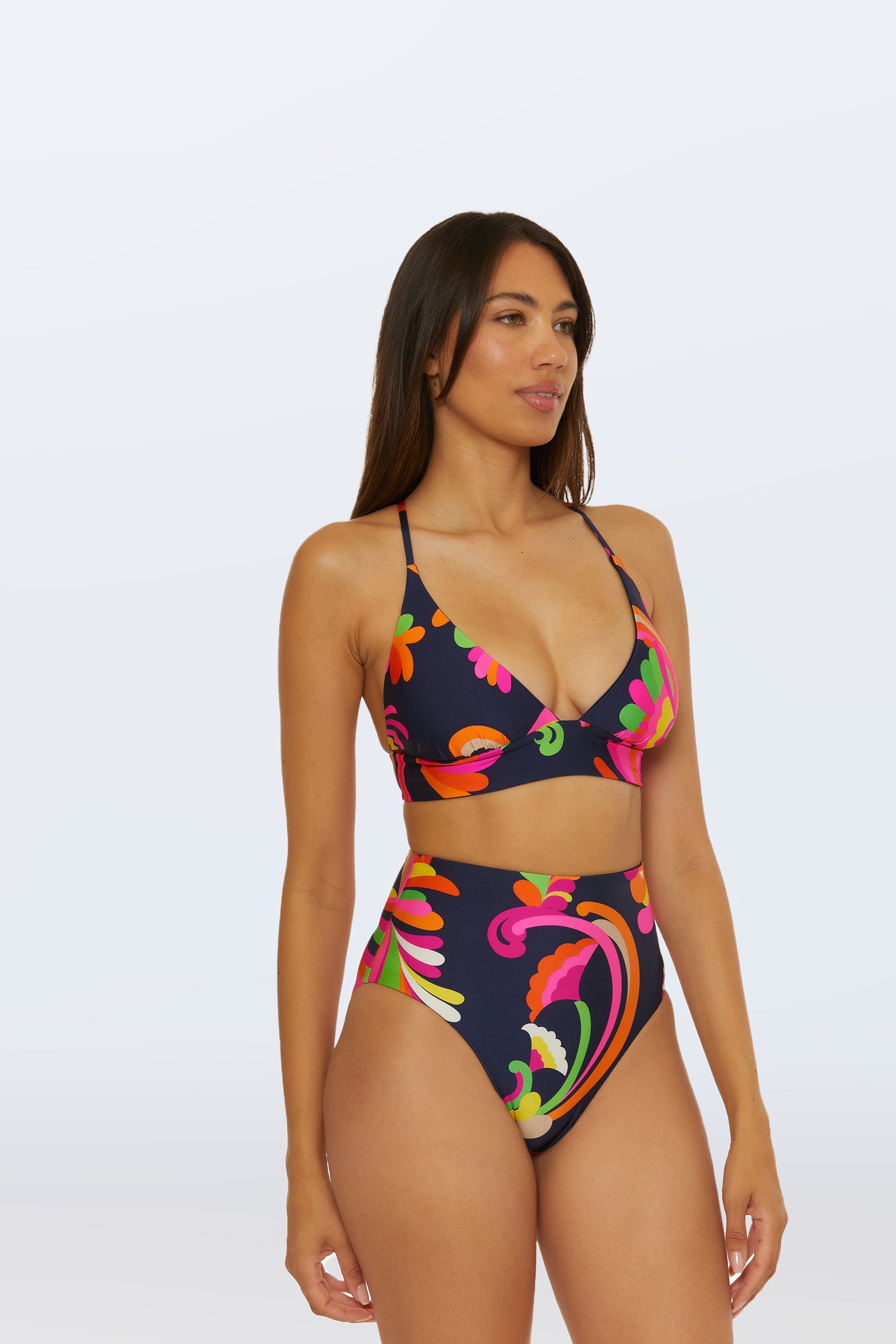 A woman models the Reversible High Waist Bottom - Palms Paradise, a dark, high-waisted bikini bottom with a vibrant pink, orange, green, and yellow swirling floral pattern, standing confidently against a plain light background.