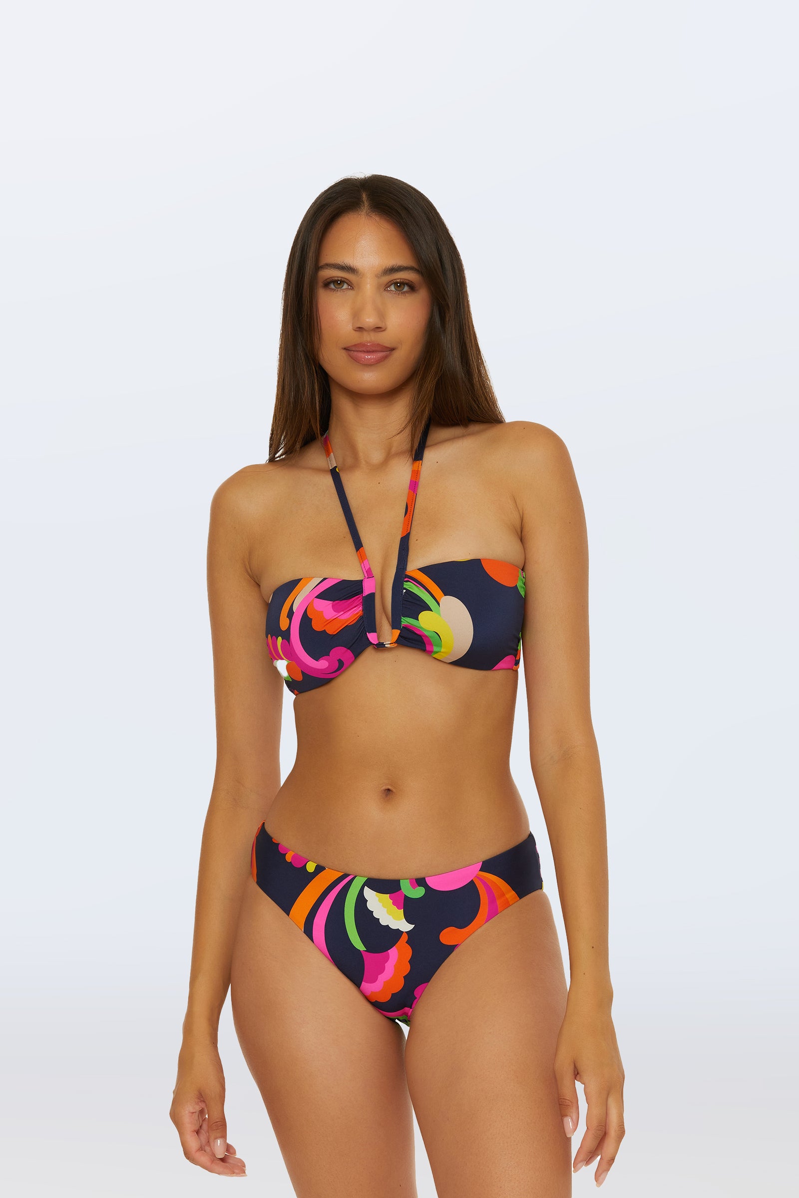 A woman wears the Bandeau Swim Top - Palms Paradise in Multi, featuring a colorful abstract pattern and a halter strap detail, standing against a light background.