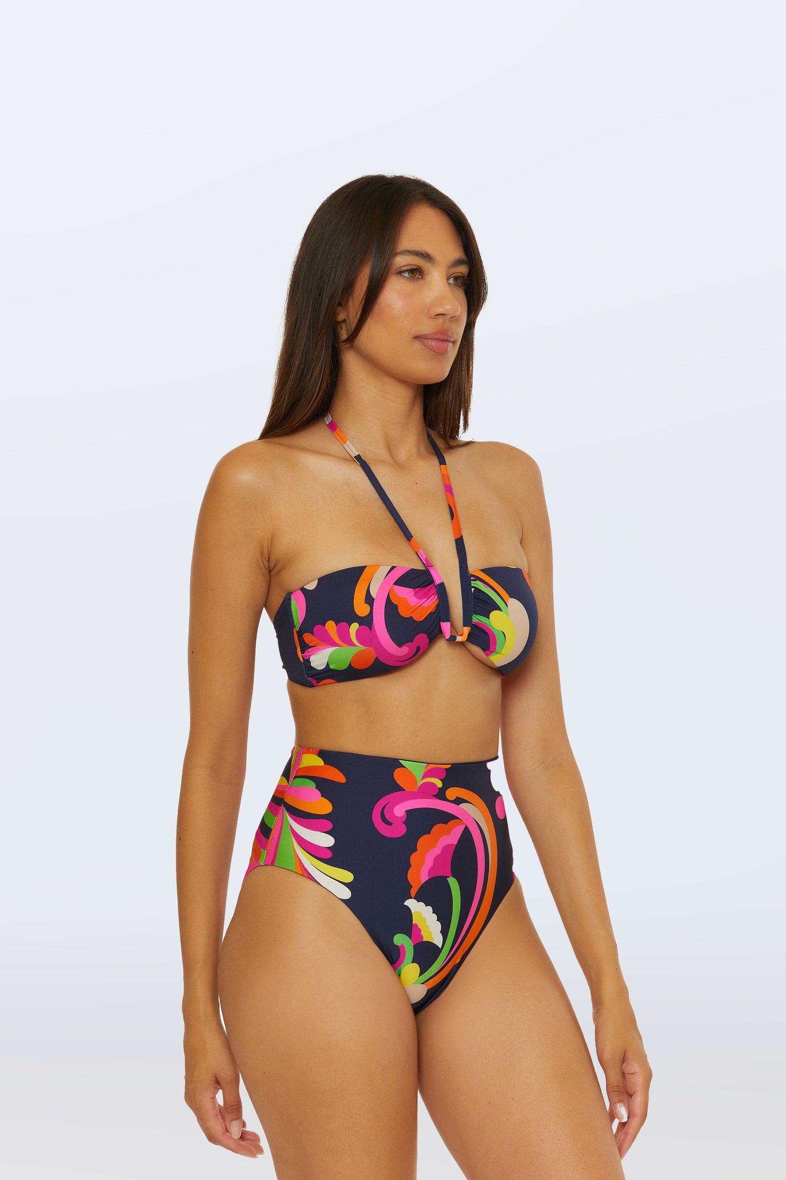 Woman wearing the Bandeau Swim Top - Palms Paradise, a colorful, abstract-patterned, high-waisted bikini with a strapless top and halter neck strap, standing against a plain light background.