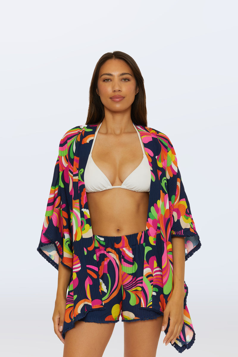A woman wears the Kimono Swim Cover-Up - Palms Paradise in multi over a white bikini top and shorts, standing against a plain light background.