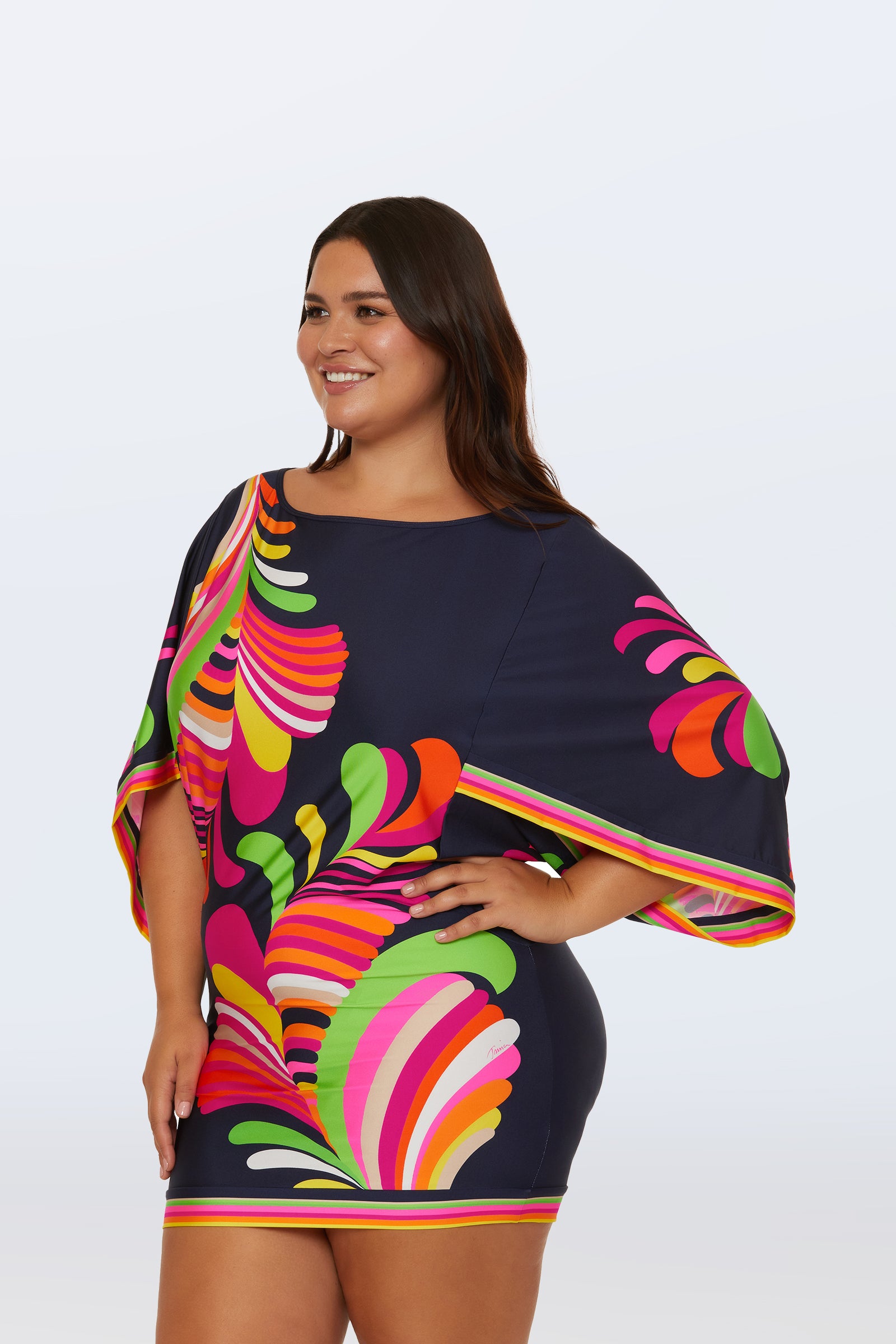 A woman smiles against a light background, wearing the Casablanca Swim Tunic - Palms Paradise, a navy blue tunic with vibrant pink, green, orange, and yellow abstract palm patterns, wide sleeves, and a short hemline.