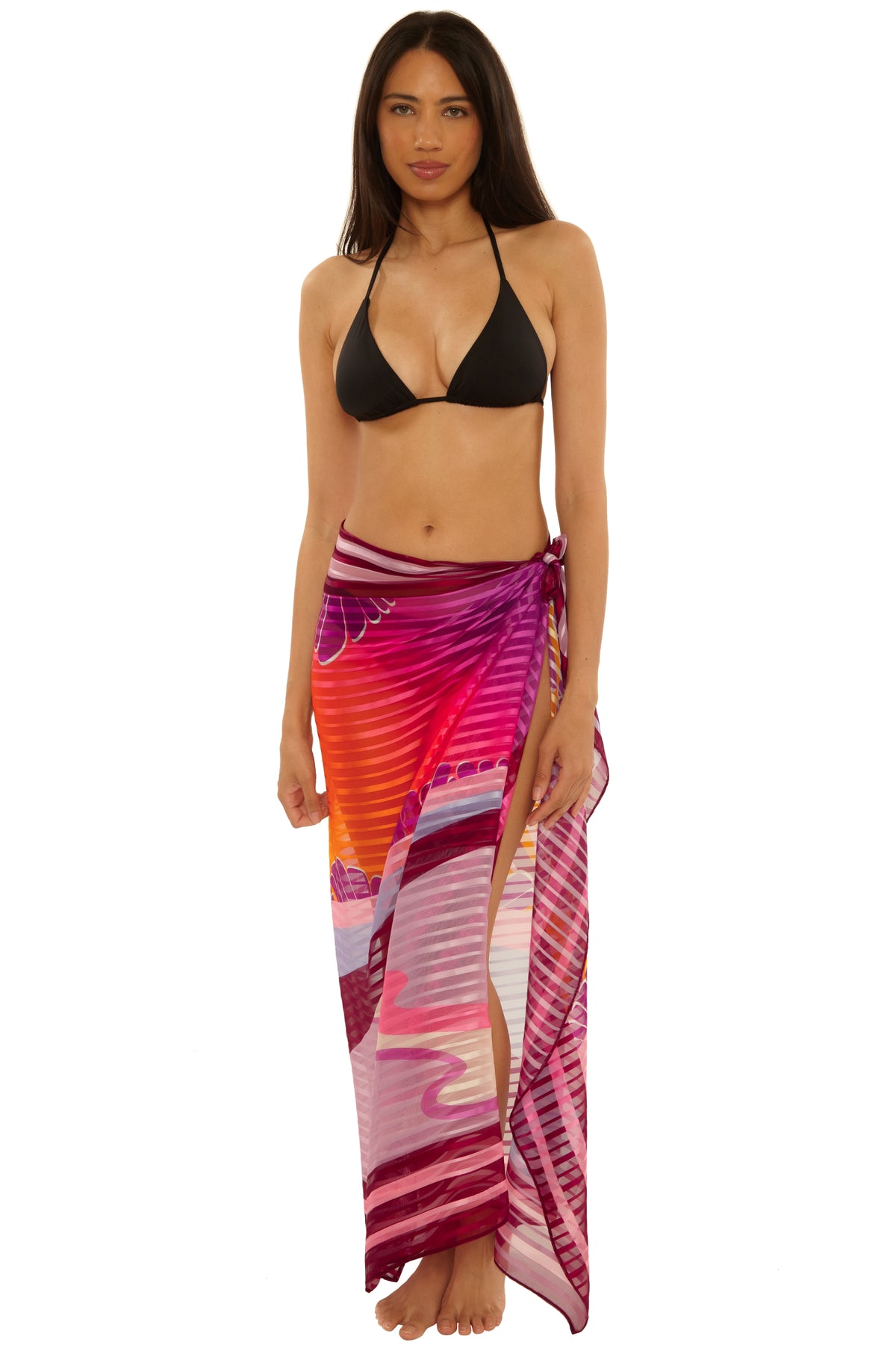 A woman stands barefoot against a white background, wearing a black bikini top and the Rhodes Pareo in MULTI, tied at the waist.