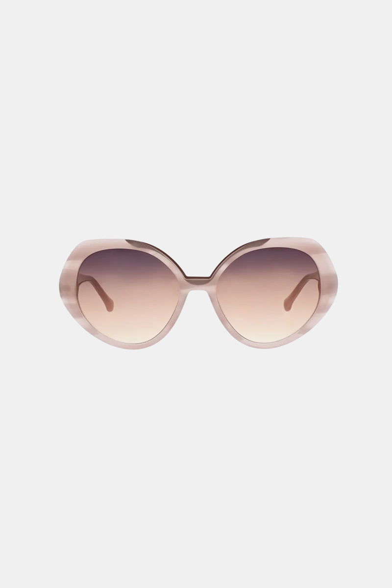 The Sandcut Sunglass features oversized, round frames in light pink with brown gradient lenses, shown against a plain white background.