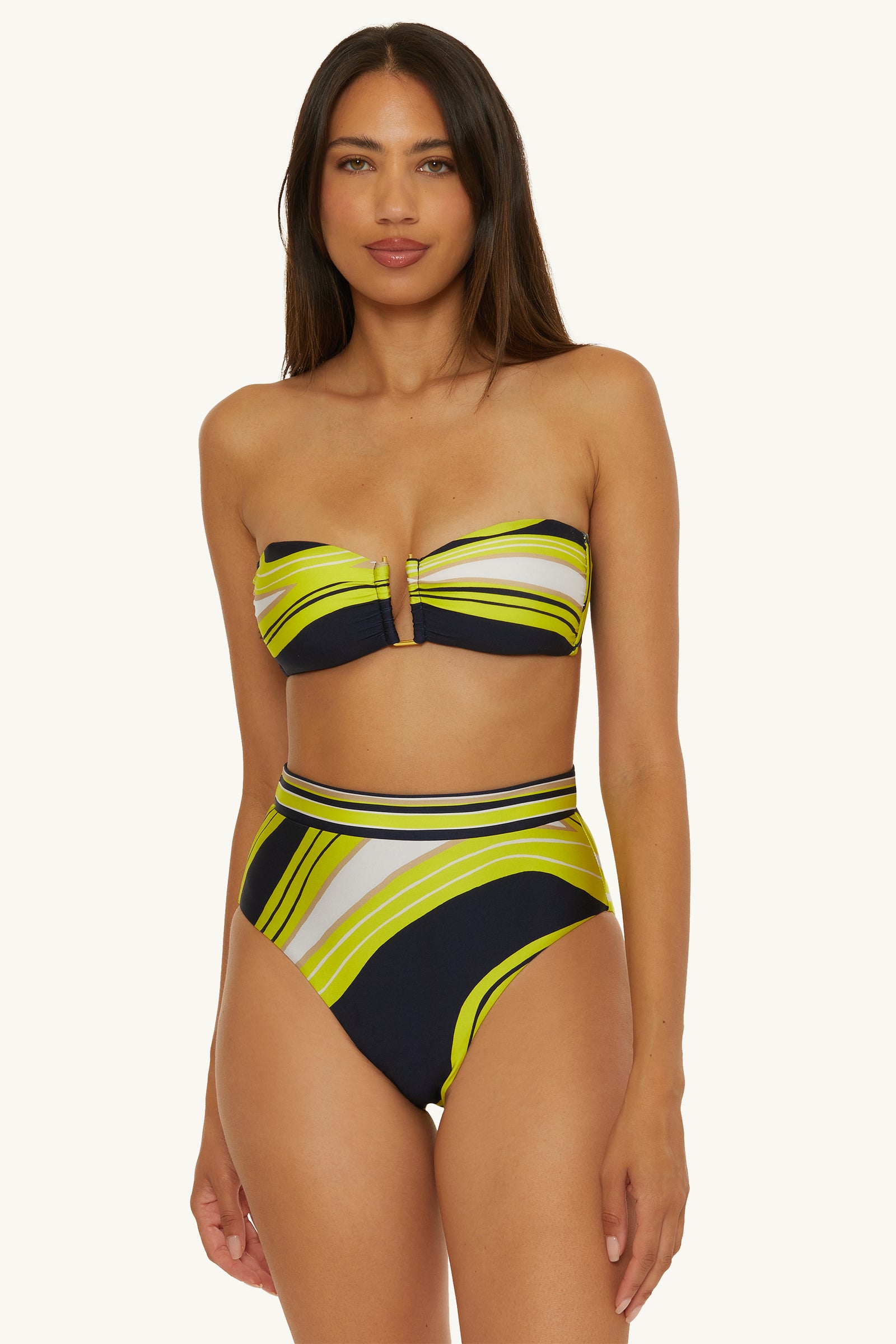 A woman wears the Strapless Bandeau Swim Top - Serena Swirl with high-waisted bottoms, featuring a yellow, green, white, and navy abstract swirl pattern, standing against a plain light background.