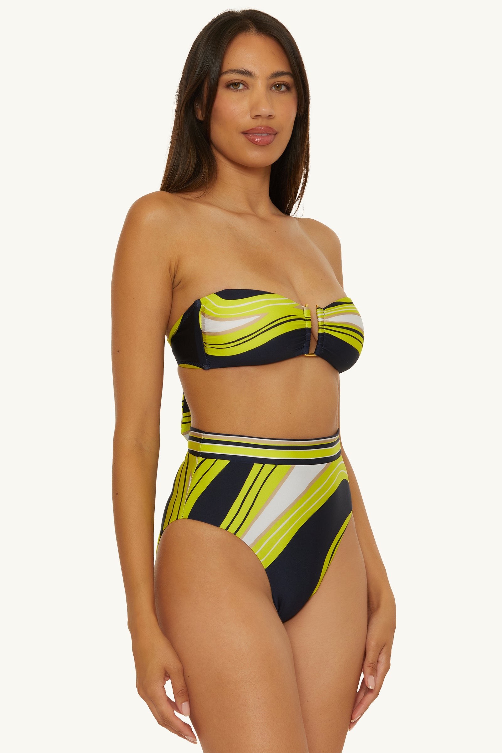 A woman with long brown hair models the Strapless Bandeau Swim Top - Serena Swirl, featuring a navy, white, and yellow-green diagonal striped pattern and a high-waisted bottom, against a plain light background.