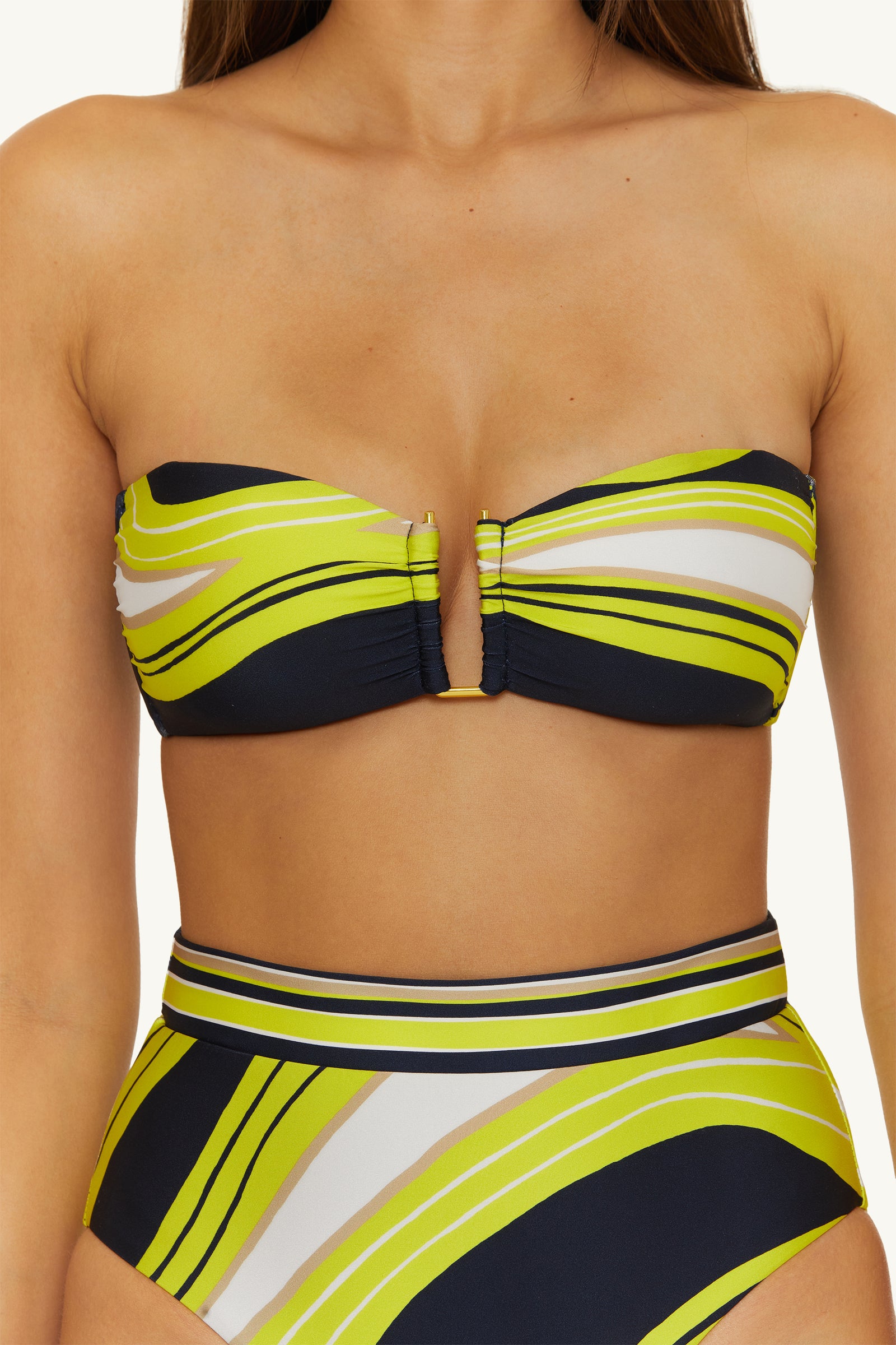A woman wears the Strapless Bandeau Swim Top - Serena Swirl, featuring a strapless design, center cutout, and high-waisted bottoms with a yellow, white, black, and green swirling stripe pattern.