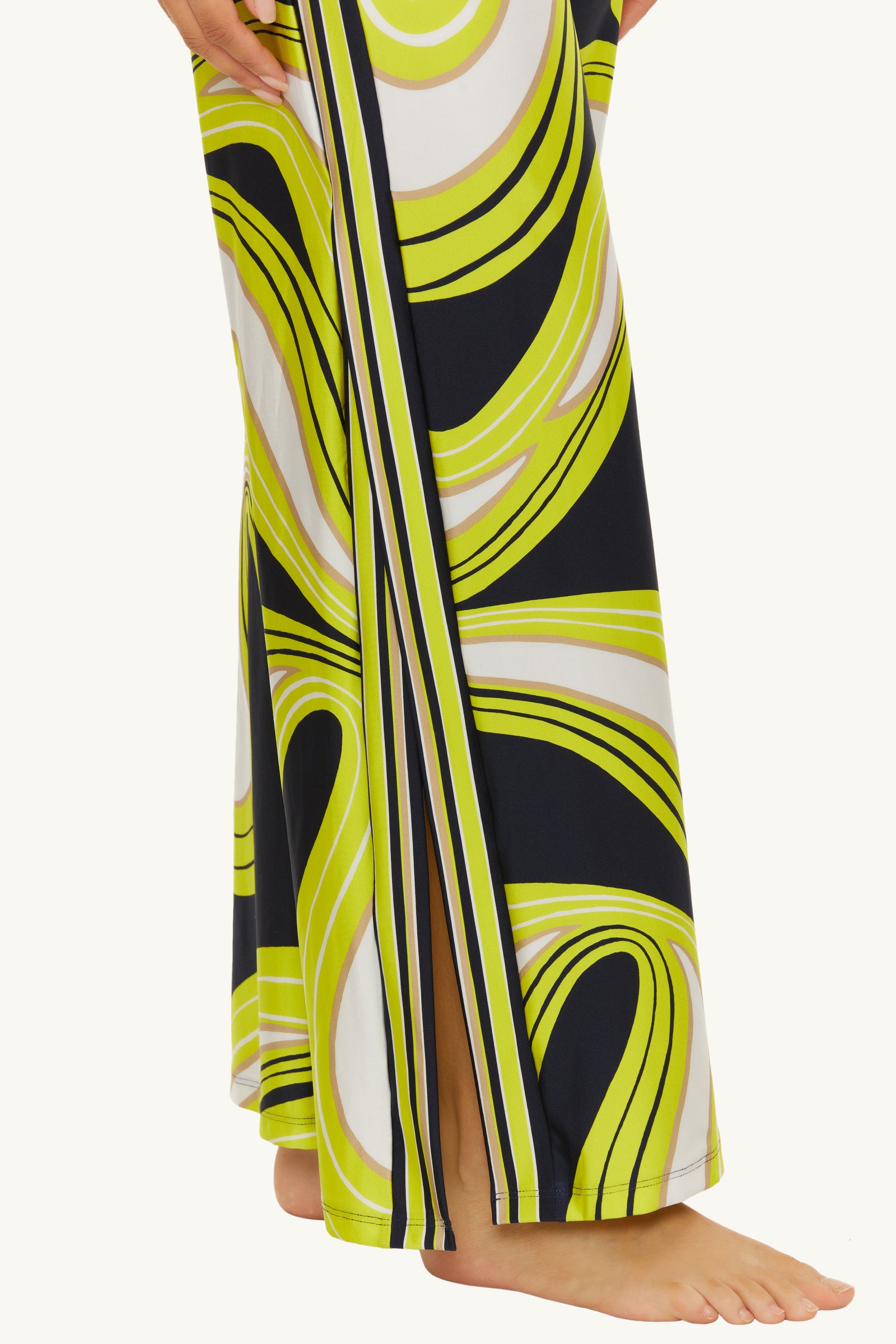 A person wearing the Serena Swirl Swim Cover-Up Pant with bold yellow, black, and white swirling patterns stands barefoot, toes peeking from beneath the hem.