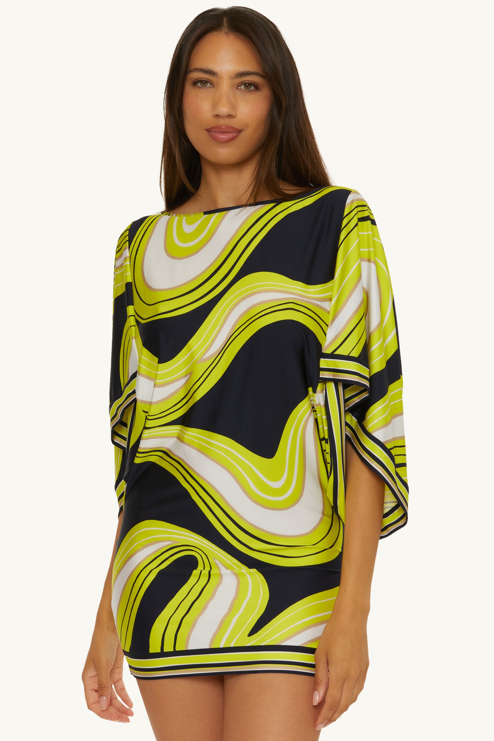 A woman models the Casablanca Tunic Cover-Up – Serena Swirl, a loose, short dress with wide sleeves and a bold yellow, white, and black abstract swirl pattern, set against a plain light background.