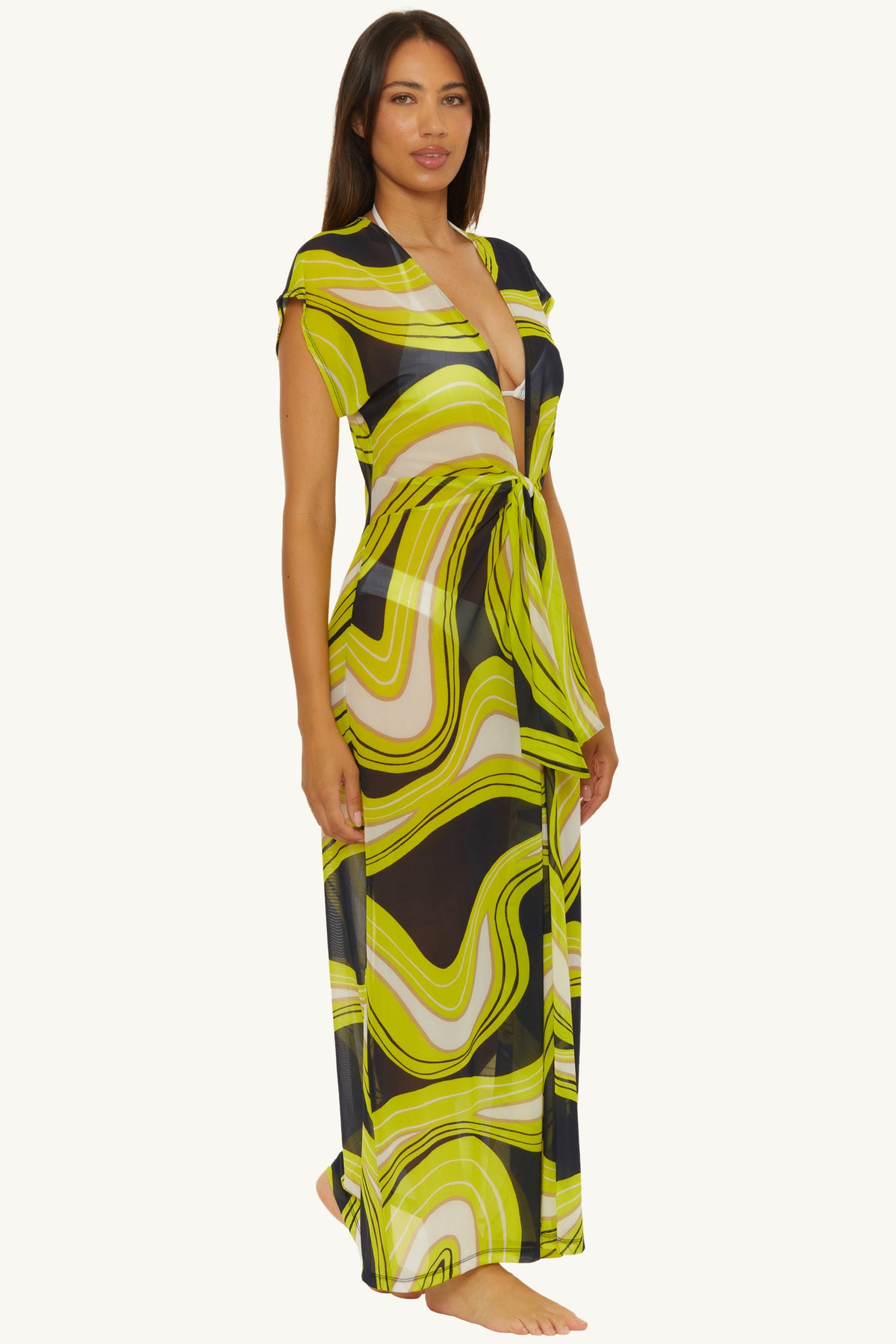 A woman stands barefoot against a plain background, wearing the Mesh Tie-Front Maxi Dress Cover-Up – Serena Swirl, a long, sheer yellow and black abstract swirl-patterned dress with a waist tie.