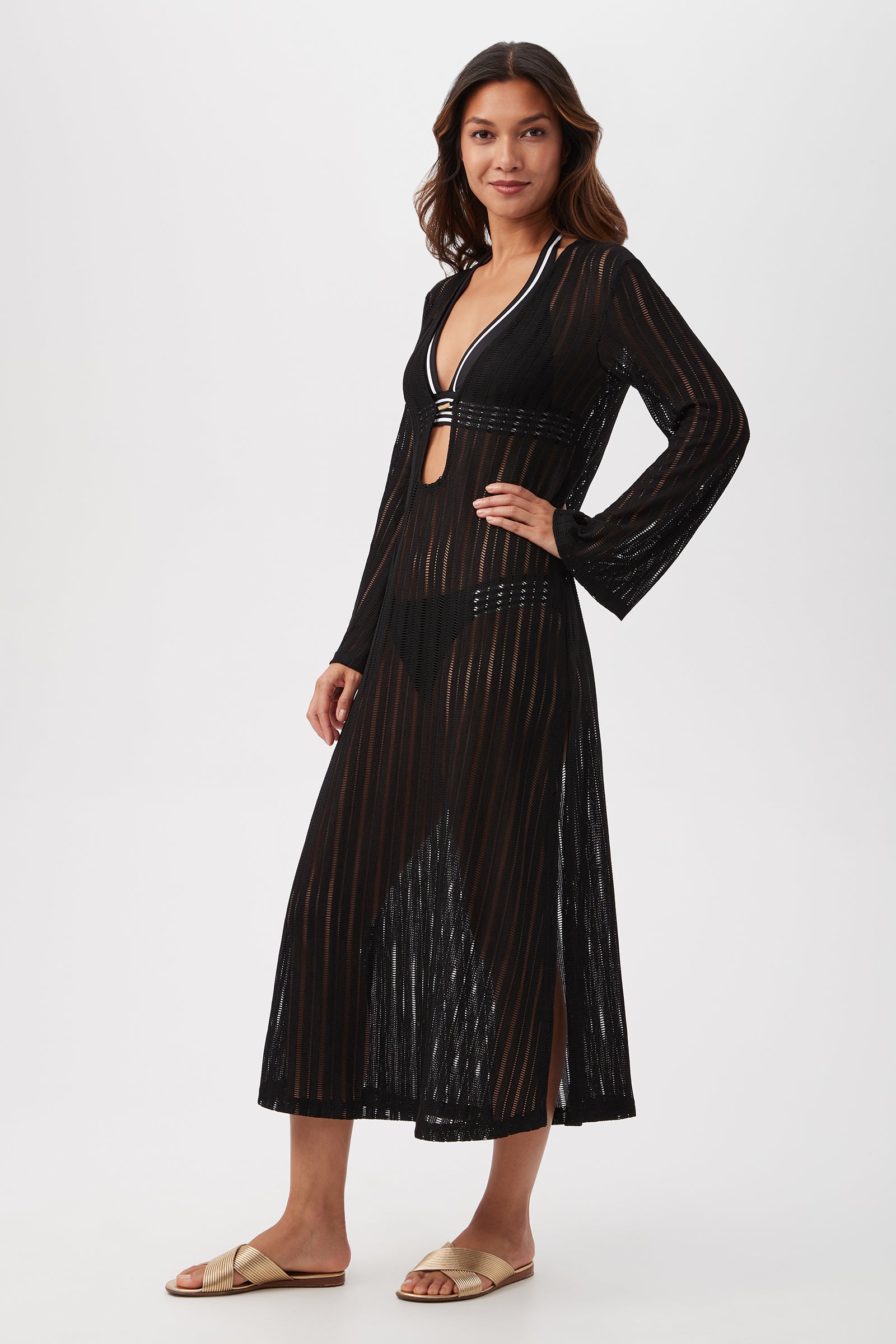 Woman stands smiling in a Skyhigh Long-Sleeve Mesh Maxi Dress Cover-Up with sheer black vertical stripes over a black bikini, beige slide sandals, and long hair, set against a plain white background.