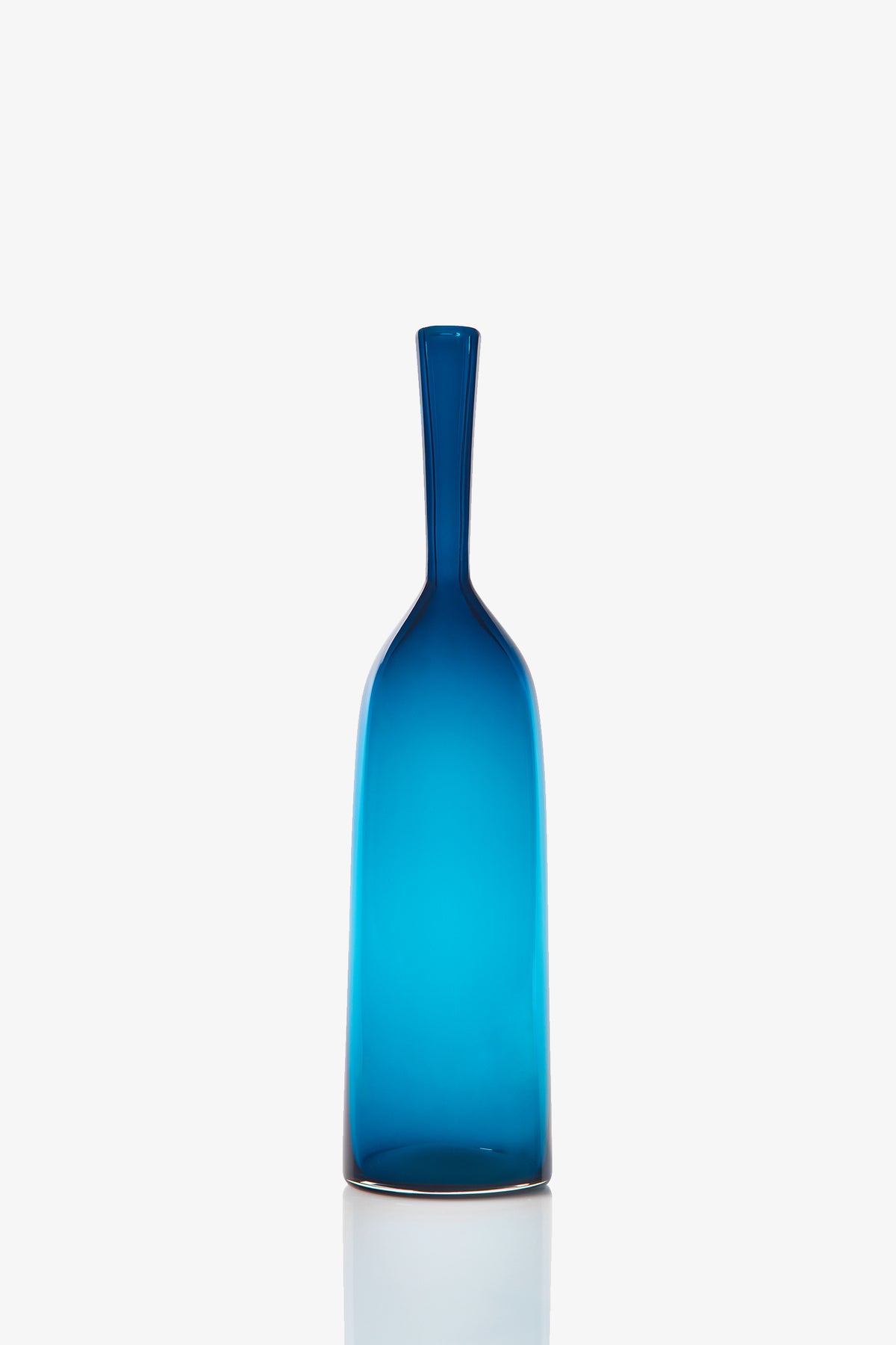 The Small Angelic Bottle is a slender blue glass bottle with a long neck and smooth surface, displayed upright on a reflective white background.