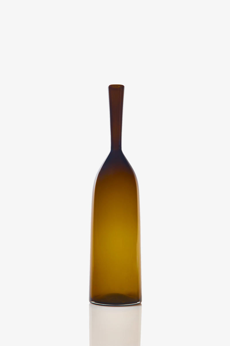 The Small Angelic Bottle is a tall, slender brown glass bottle with a narrow neck and smooth surface, shown against a plain white background and casting a soft reflection below.