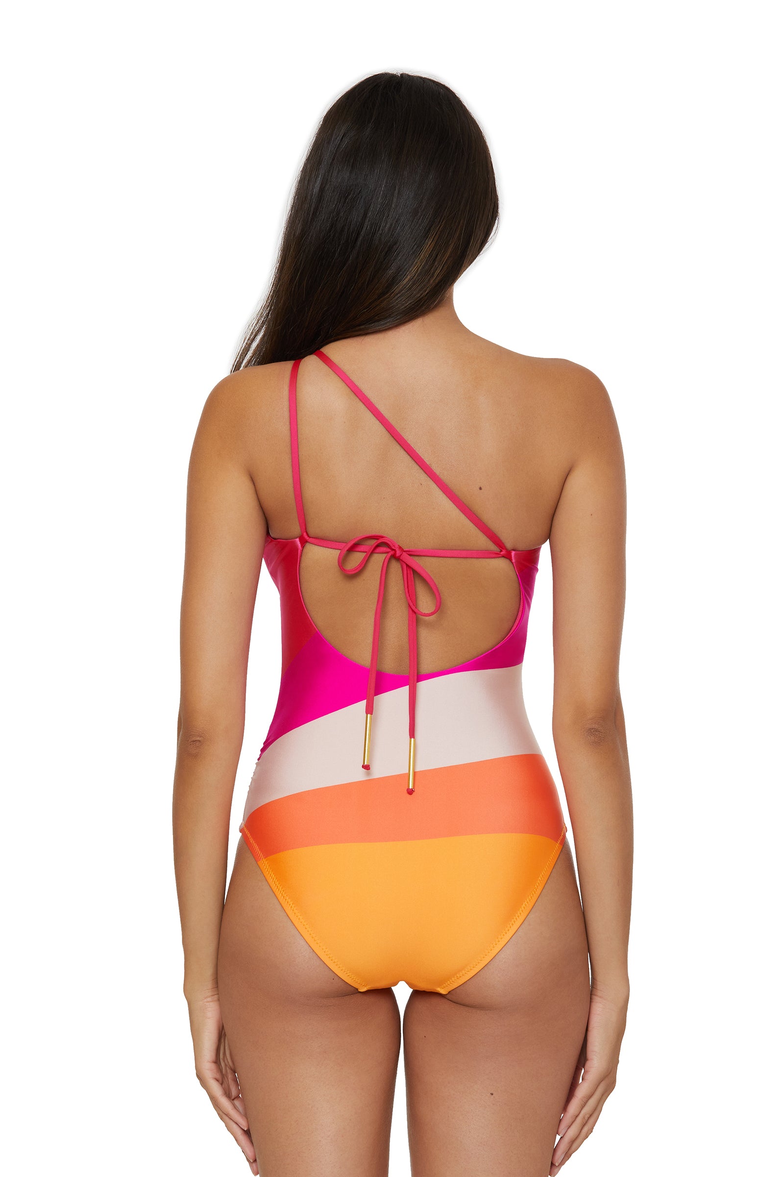 A woman with long brown hair is seen from behind wearing the Sunburst One-Shoulder One-Piece Swimsuit, which features vibrant pink, red, white, orange, and yellow stripes, a back cutout, and a tie with gold tips.
