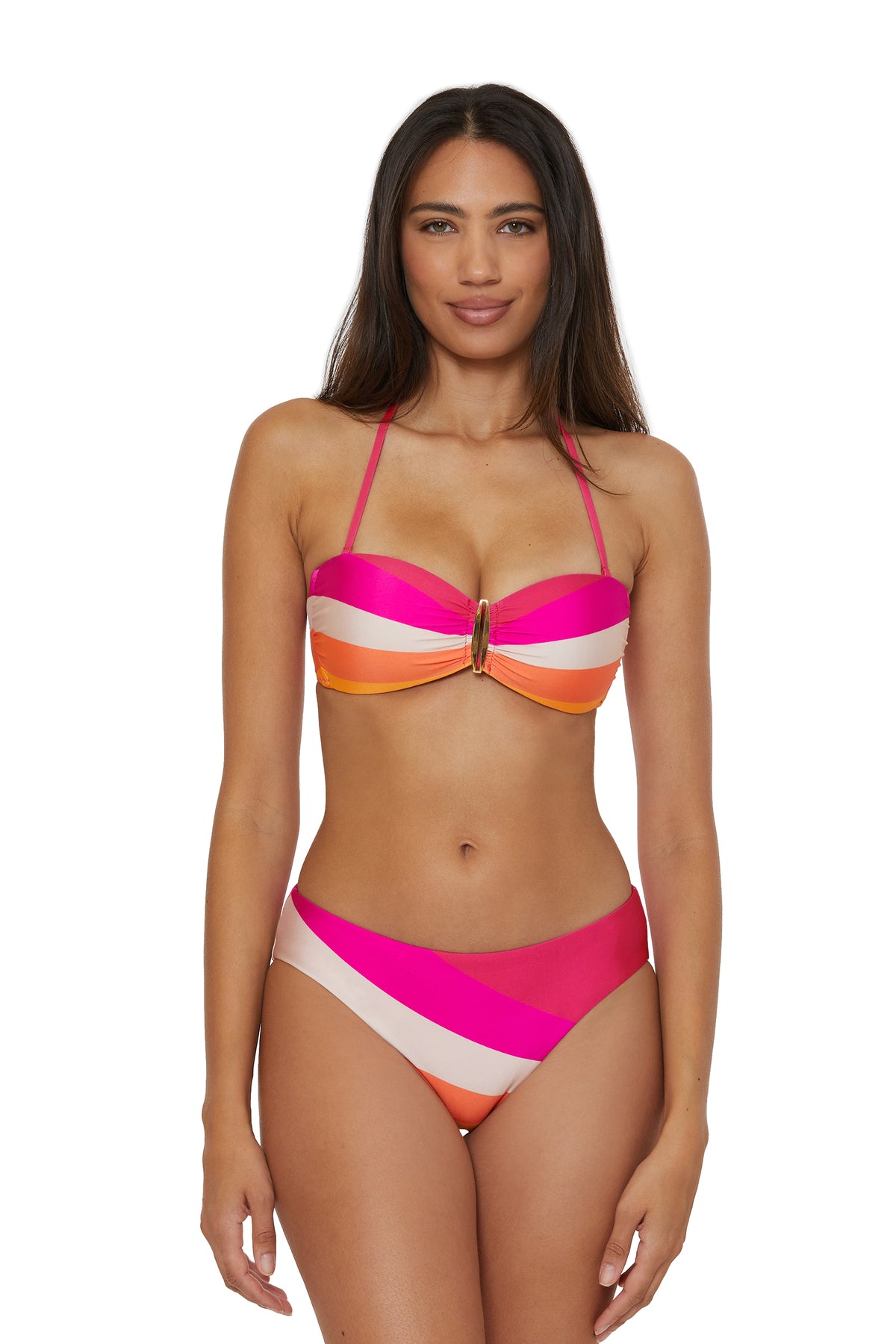 A woman with long dark hair wears the Buckle Bandeau Swim Top in Sunburst, featuring colorful stripes of pink, orange, and white, as she stands smiling at the camera against a plain white background.