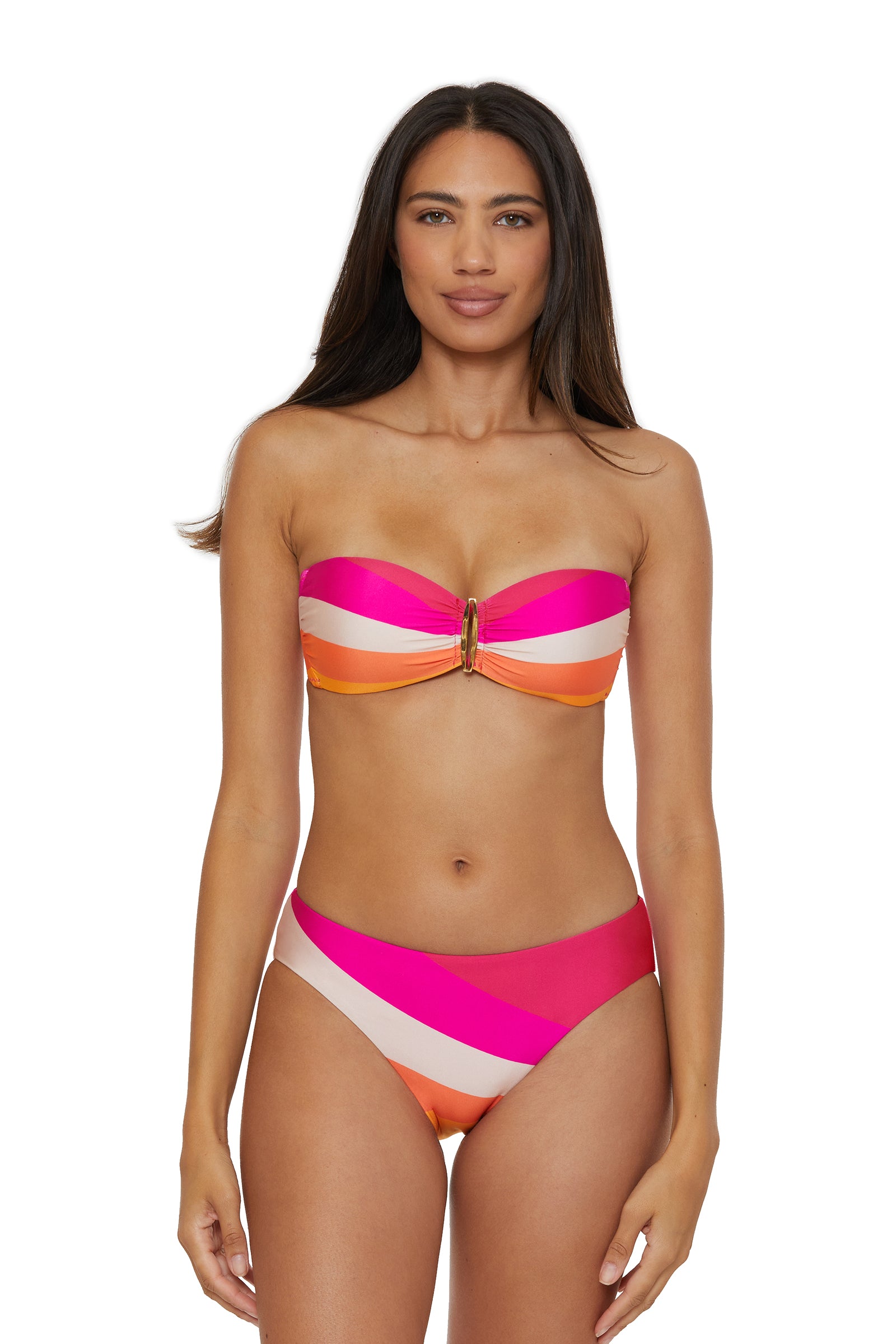 A woman faces forward wearing the Buckle Bandeau Swim Top - Sunburst, a strapless bikini with bold diagonal stripes in pink, orange, white, and red plus a gold center accent. She has long dark hair and a neutral expression.