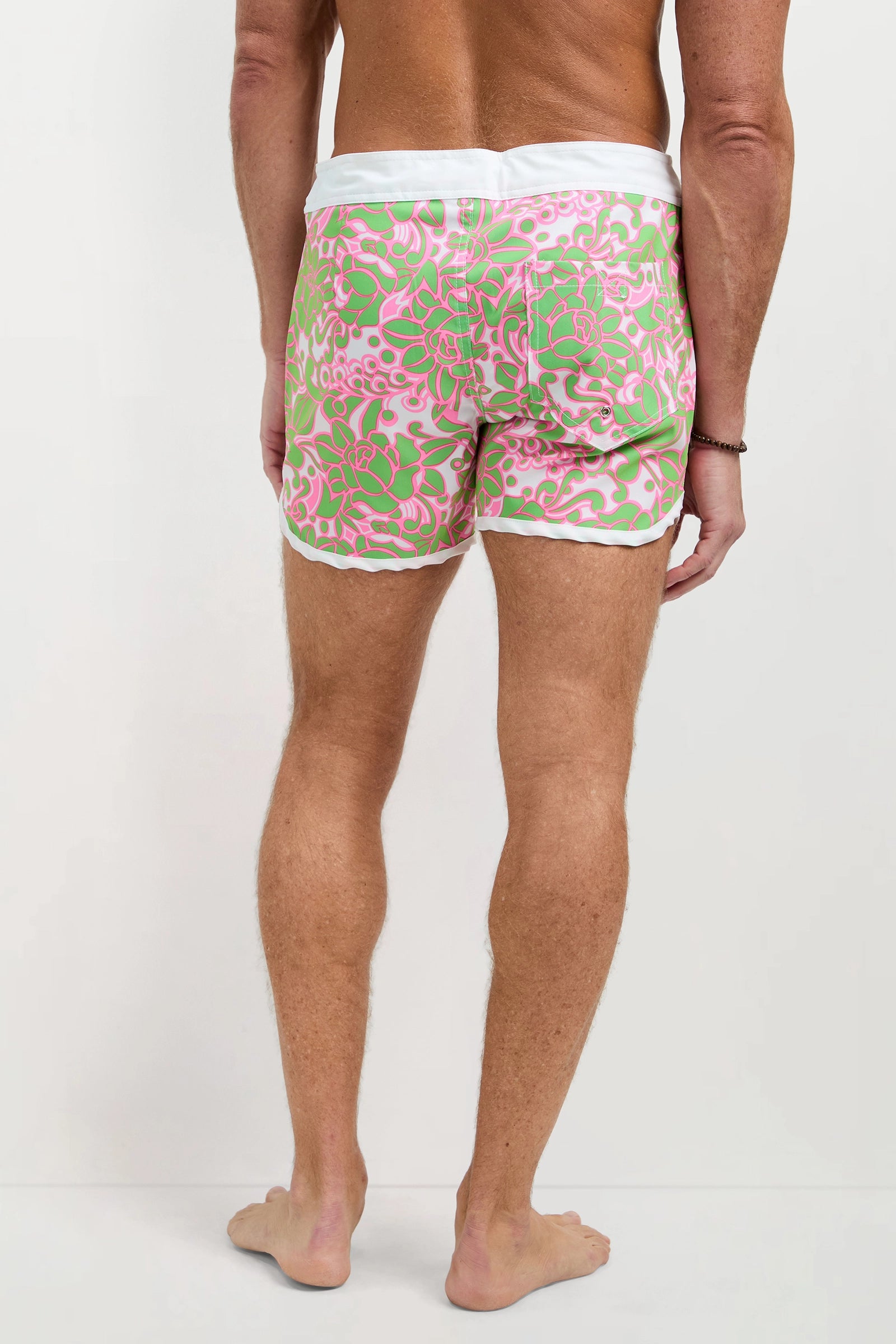 A man is barefoot, facing away from the camera, wearing the Surfside Board Short - Petra Floral with a white waistband and trim, set against a plain white background.