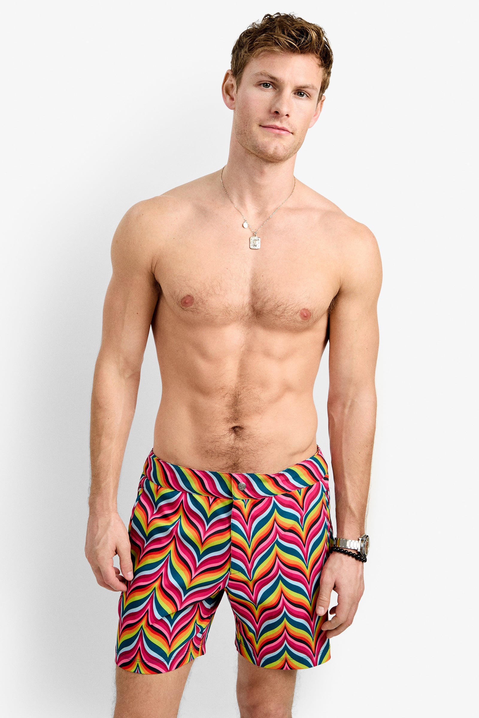 A shirtless man with a light build and short brown hair models the Honolulu Board Short - Chelsea Chevron against a plain white background, accessorized with a necklace and a watch.