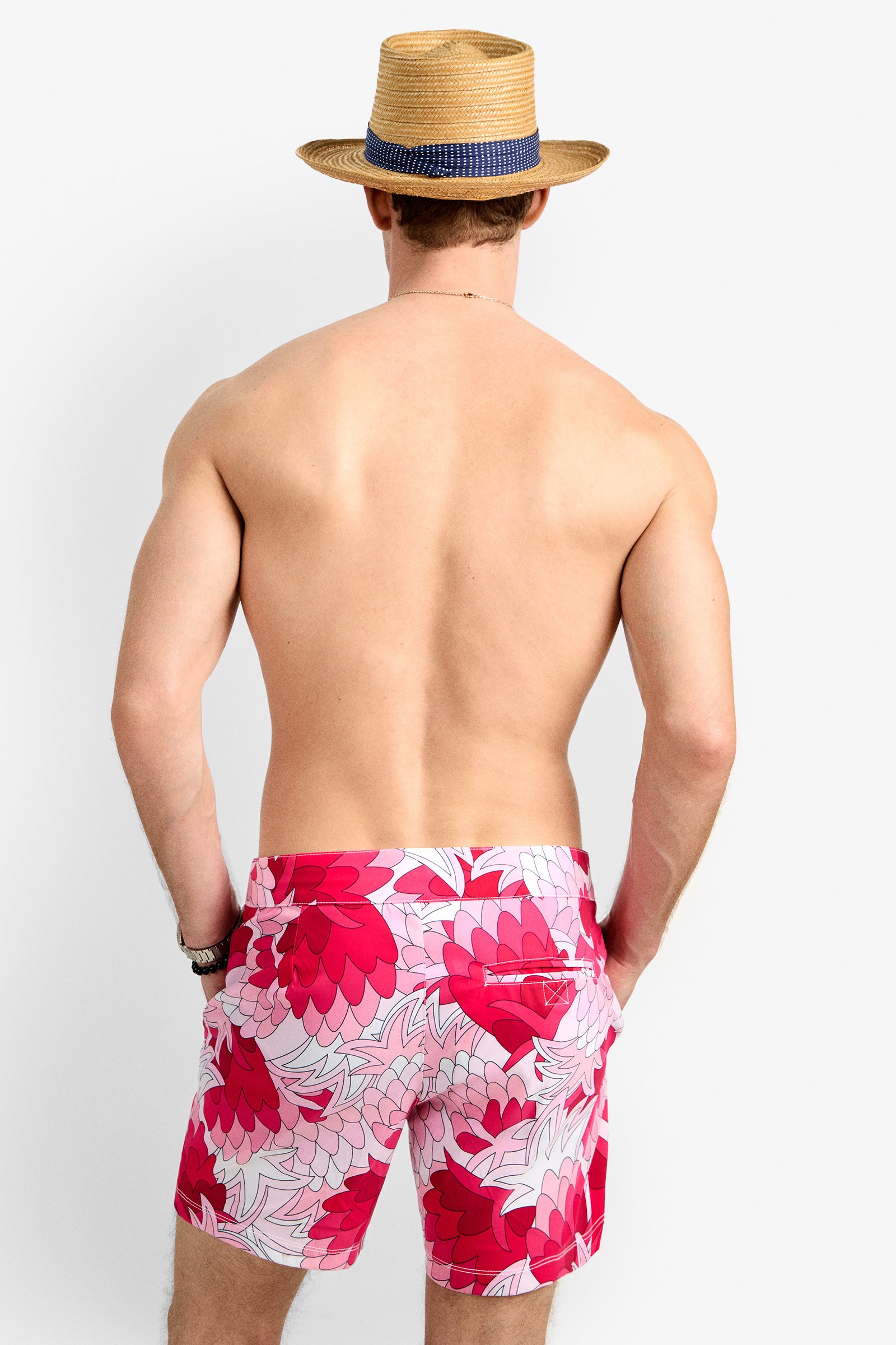 A shirtless man wearing the Honolulu Board Short, featuring pink and red floral prints, stands with his back to the camera against a plain white background.