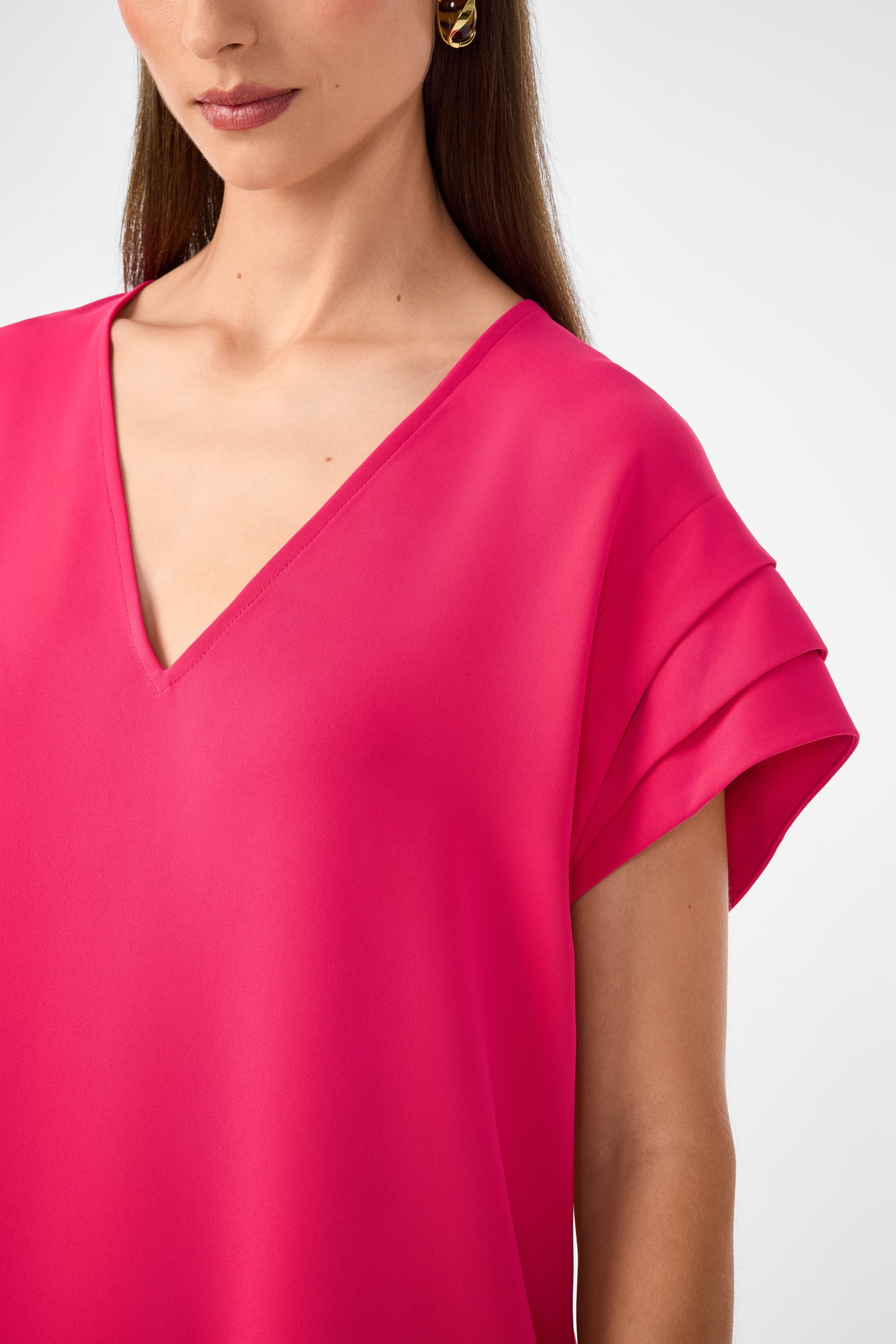 A woman with long brown hair and gold hoop earrings wears the Sadora Short-Sleeve Dress in bright pink. Only her lower face, neck, and upper torso are visible.