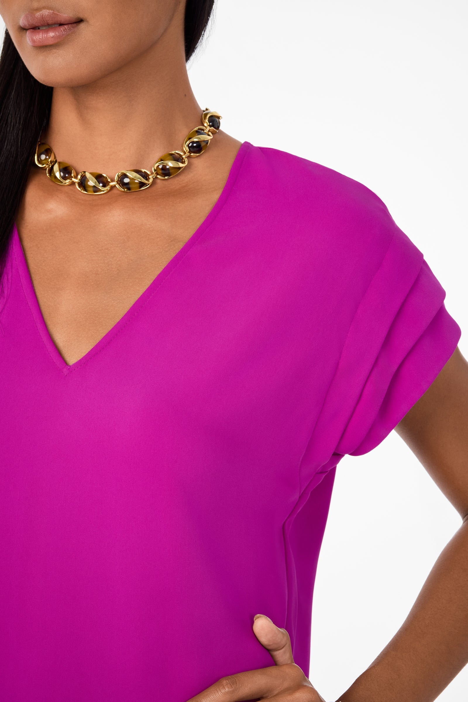A woman wears the Sadora Short-Sleeve Dress in vibrant geranium, accessorized with a chunky gold and black chain necklace, with her hand on her hip against a plain white background.